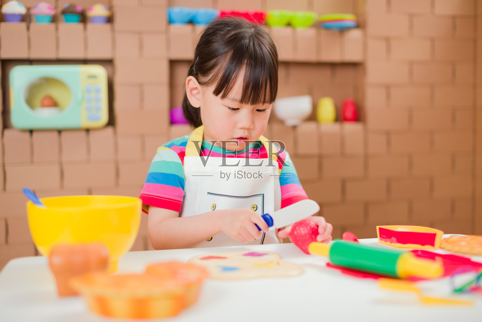 蹒跚学步的小女孩以纸板店为背景，假装扮演准备食物的角色照片摄影图片