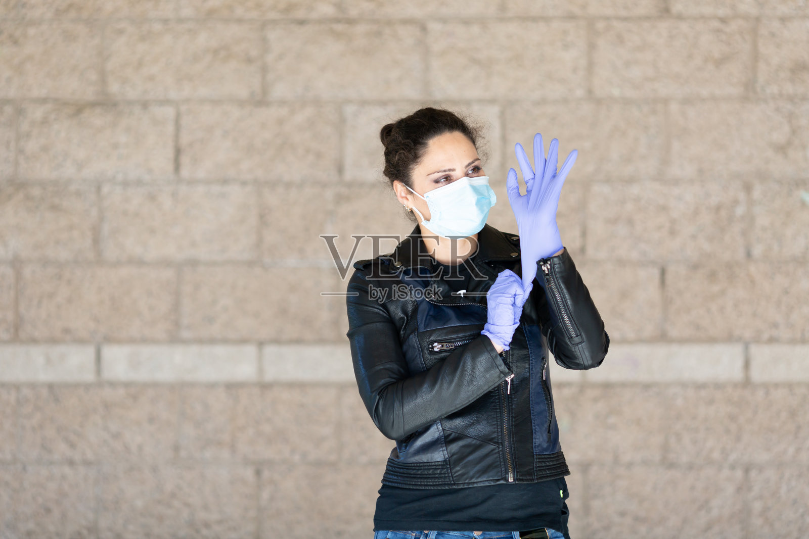 一个腰部以上的年轻白人妇女的肖像，深色卷发，戴着外科口罩和紫色乳胶手套照片摄影图片