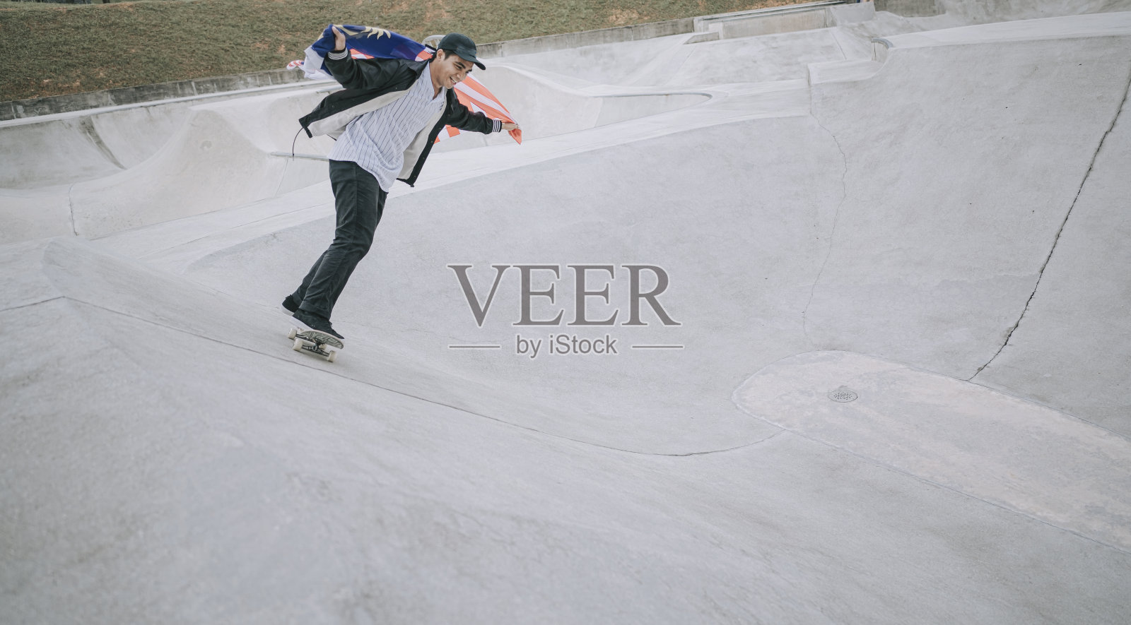 一个年轻的马来西亚男子在公园里玩滑板，手里拿着马来西亚国旗照片摄影图片