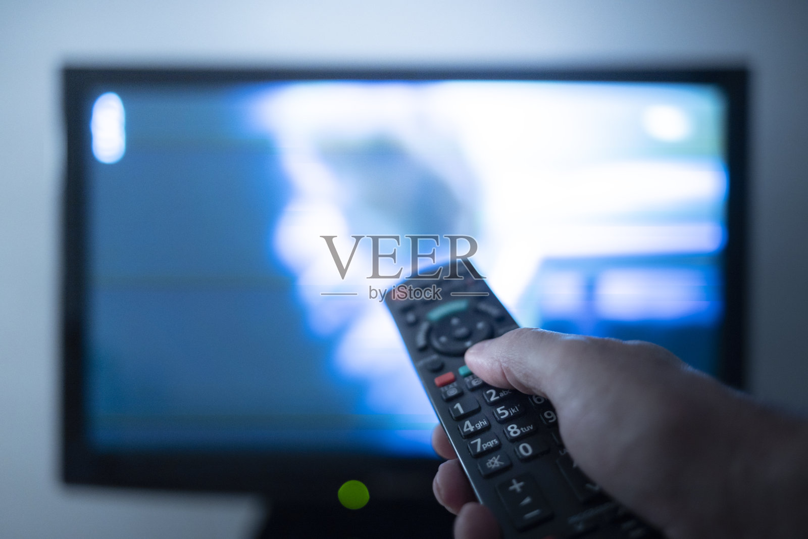 手拿遥控器坐在电视机前照片摄影图片