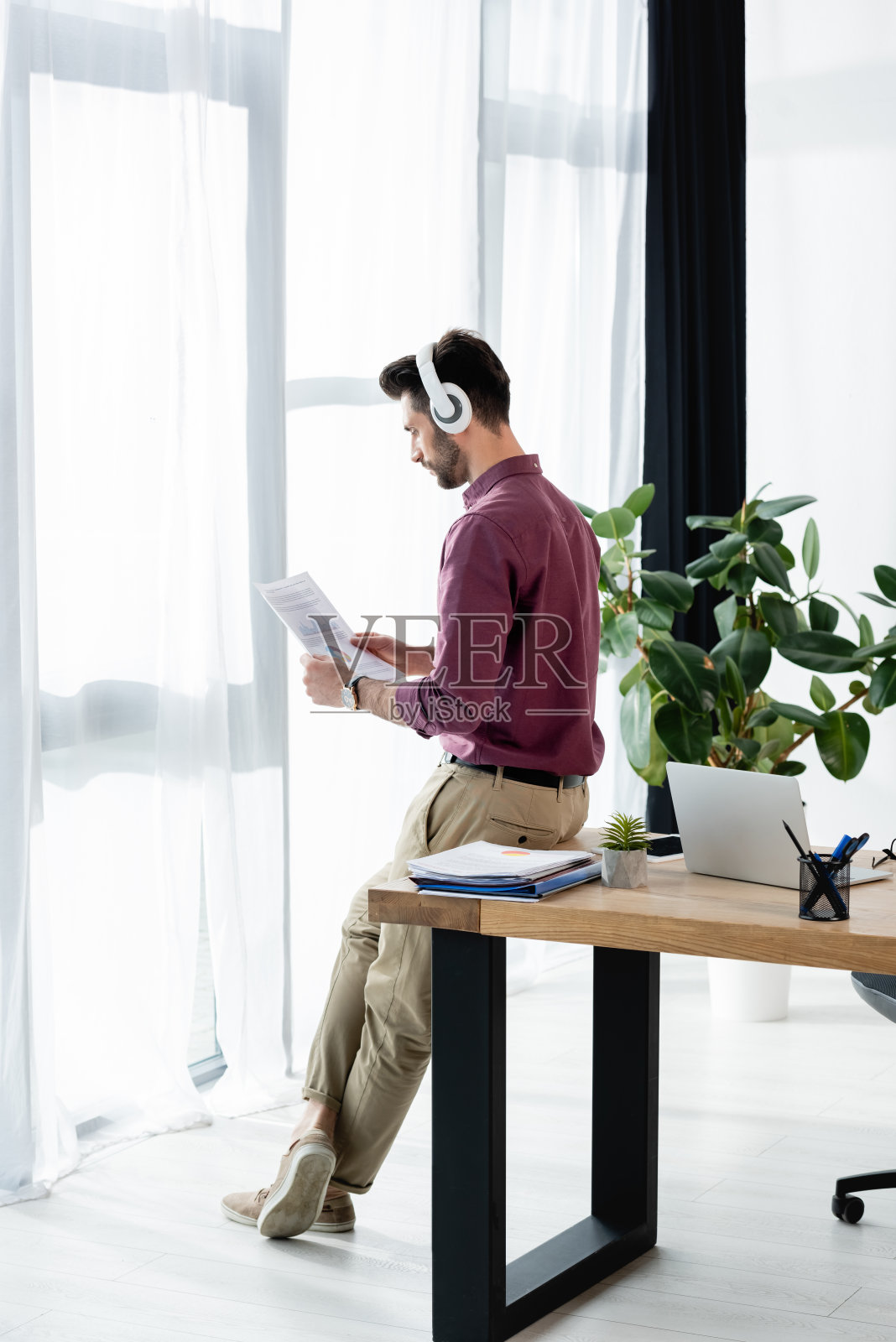 商人戴着无线耳机坐在靠窗的桌子上看文件照片摄影图片