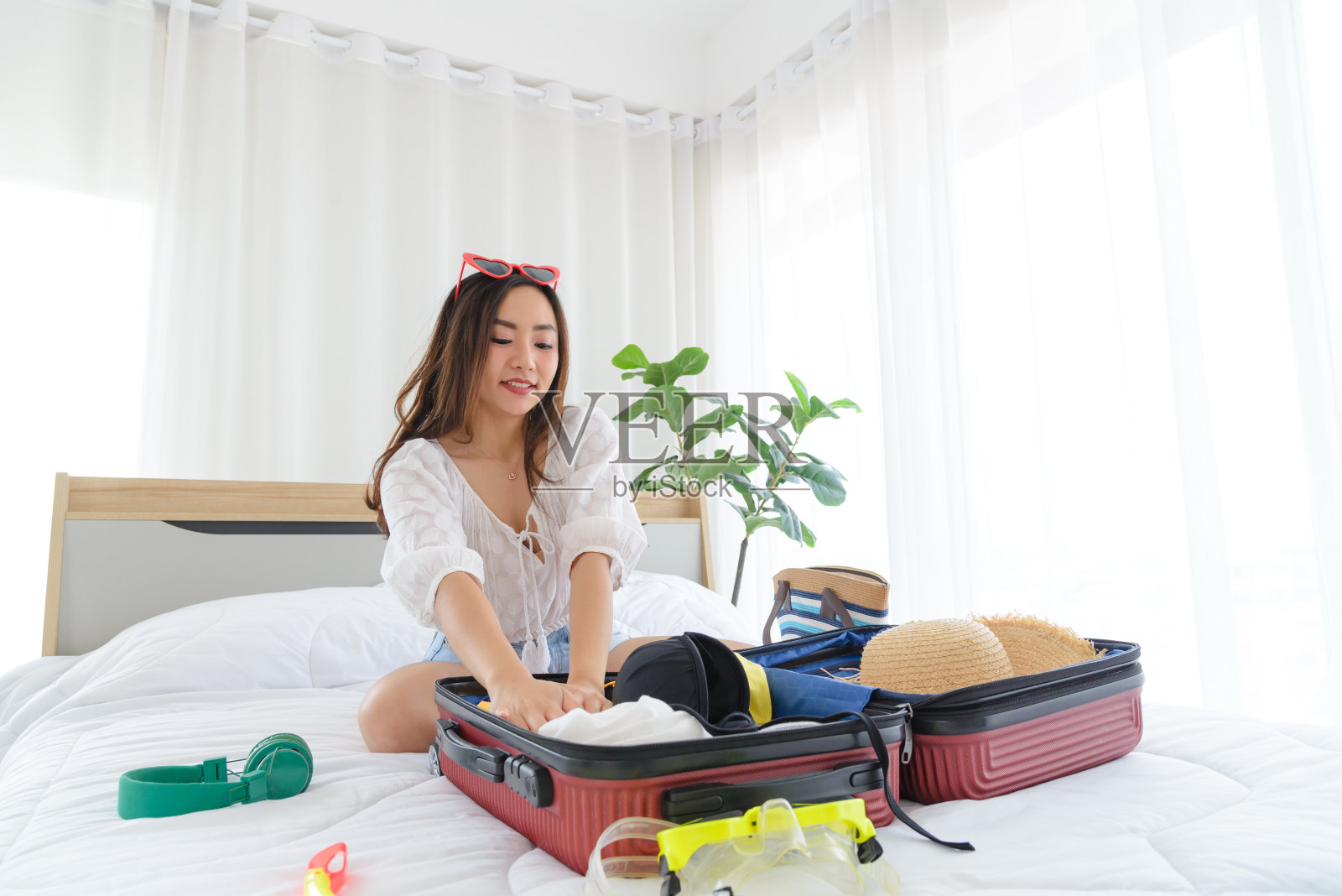 年轻的亚洲女人在床上把夏装和沙滩配件装进行李箱。为新的旅程准备旅行物品。暑假放假，假期概念。照片摄影图片