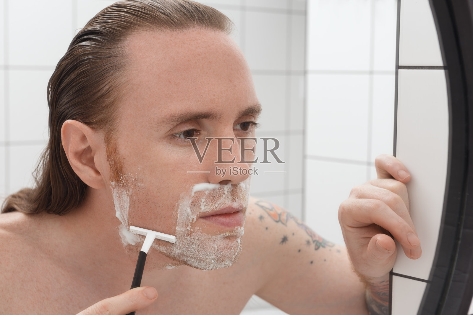 细心的长头发文身男子刮脸照片摄影图片