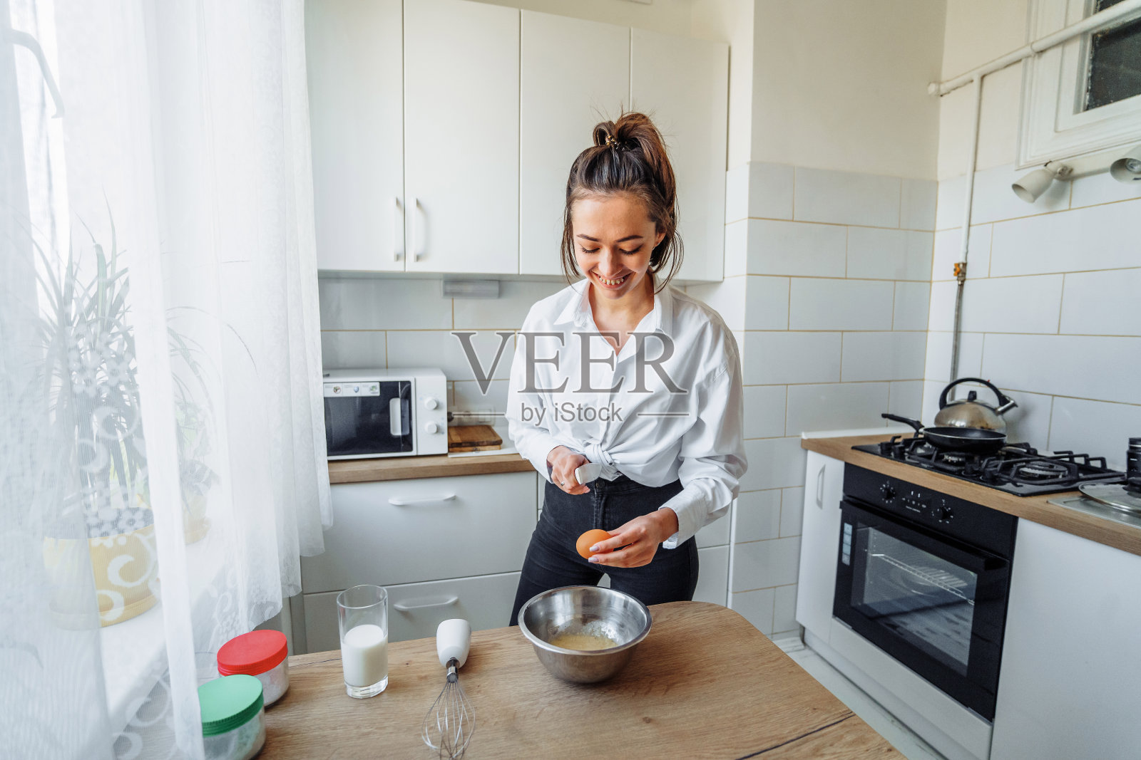 女人把面团倒进平底锅里，做自制的香蕉煎饼。爱好在一个美丽明亮的厨房。经济太太正带着美味可口的食物等着她的丈夫下班照片摄影图片