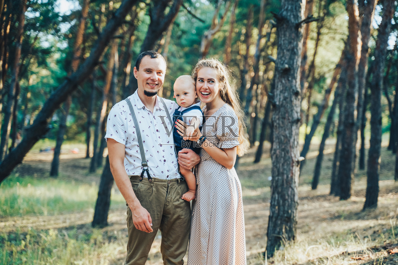 半身的肖像。一个快乐的家庭和一个一岁的男孩站在森林和微笑。穿着时尚、和谐的米色衣服。在郊外度周末。看相机照片摄影图片