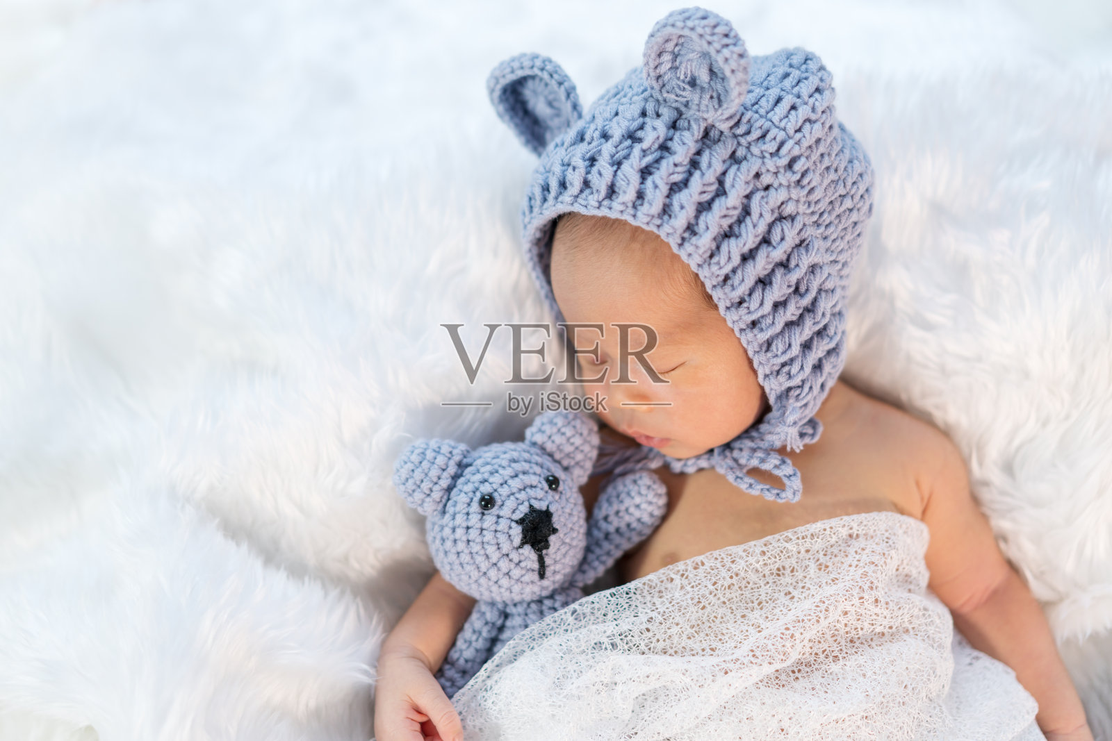 新生儿戴着熊帽睡在毛床上照片摄影图片