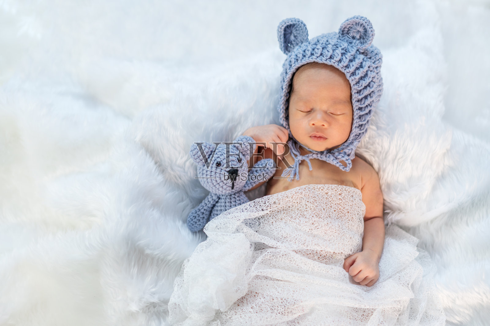 新生儿戴着熊帽睡在毛床上照片摄影图片