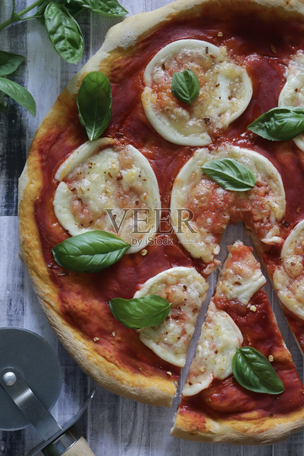 新鲜出炉的自制玛格丽塔披萨，配有披萨轮，金色的水牛马苏里拉奶酪圈，丰富的番茄番茄沙司和新鲜的罗勒叶点缀，灰色的舌和槽效果背景，俯瞰的视野照片摄影图片