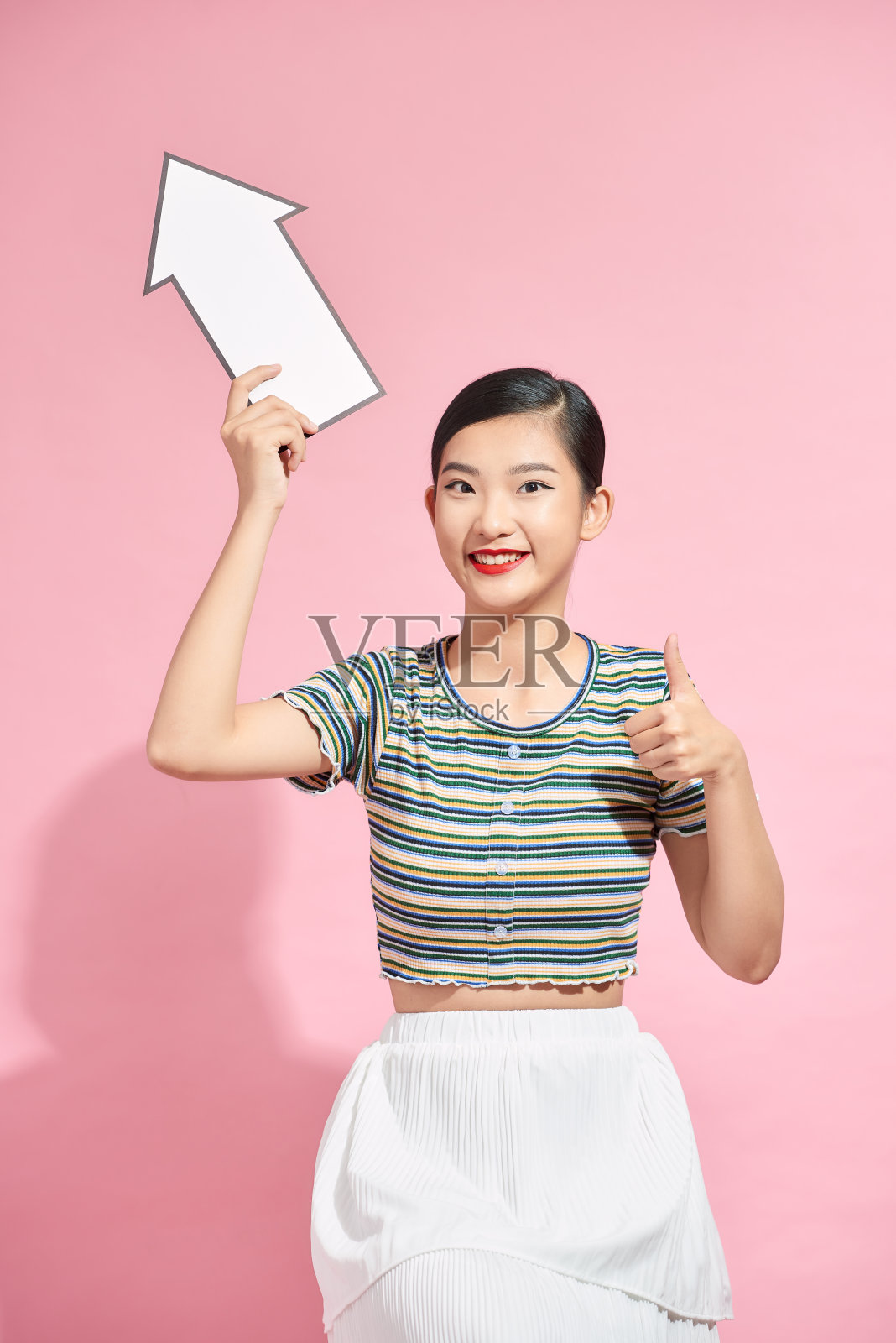 美丽兴奋的年轻女子身穿夏装孤立地站在粉红色的背景上，用箭头指向拷贝空间照片摄影图片