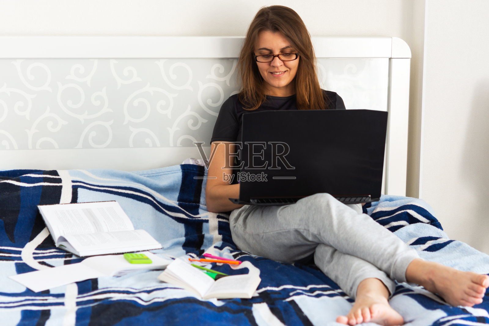 漂亮的年轻女子坐在床上用笔记本电脑照片摄影图片