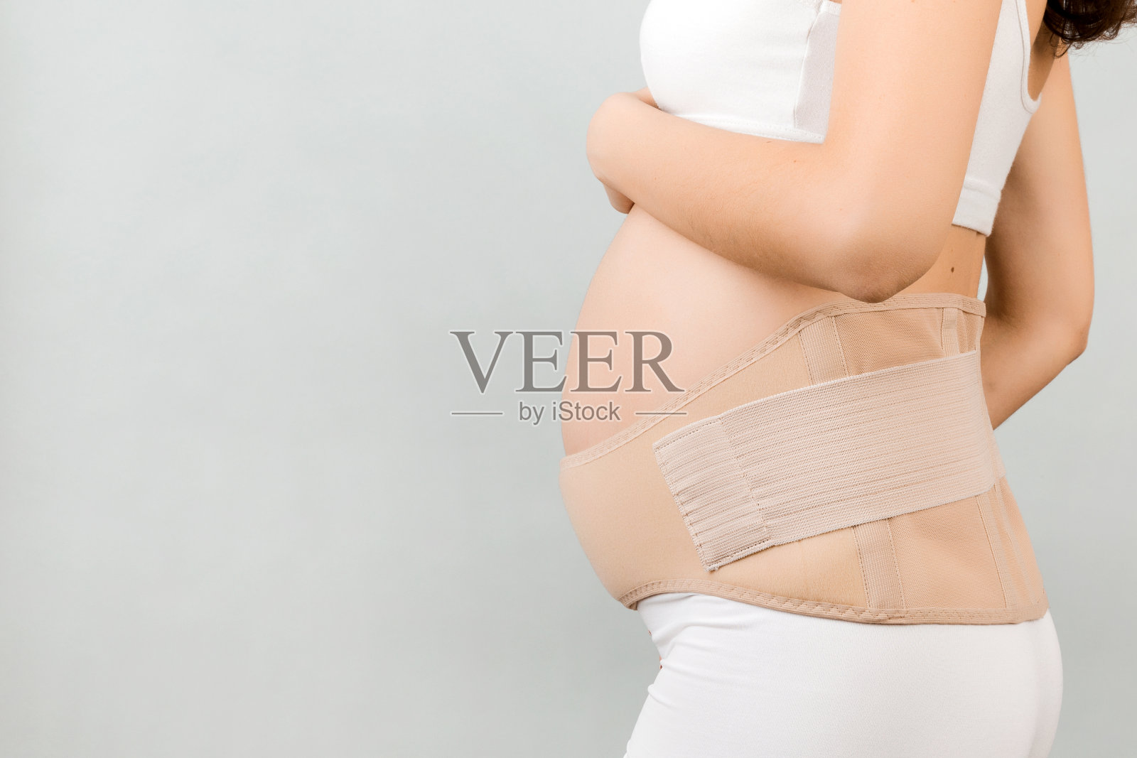 侧视图孕妇穿着内衣戴着怀孕绷带在灰色背景与拷贝空间。骨科腹部支撑带闭合概念照片摄影图片