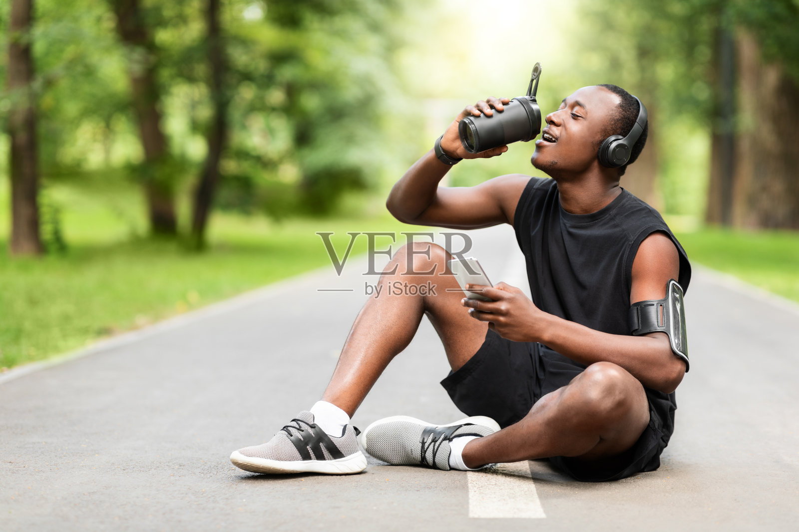 健康的黑人运动员喝着蛋白质，坐在小路上照片摄影图片