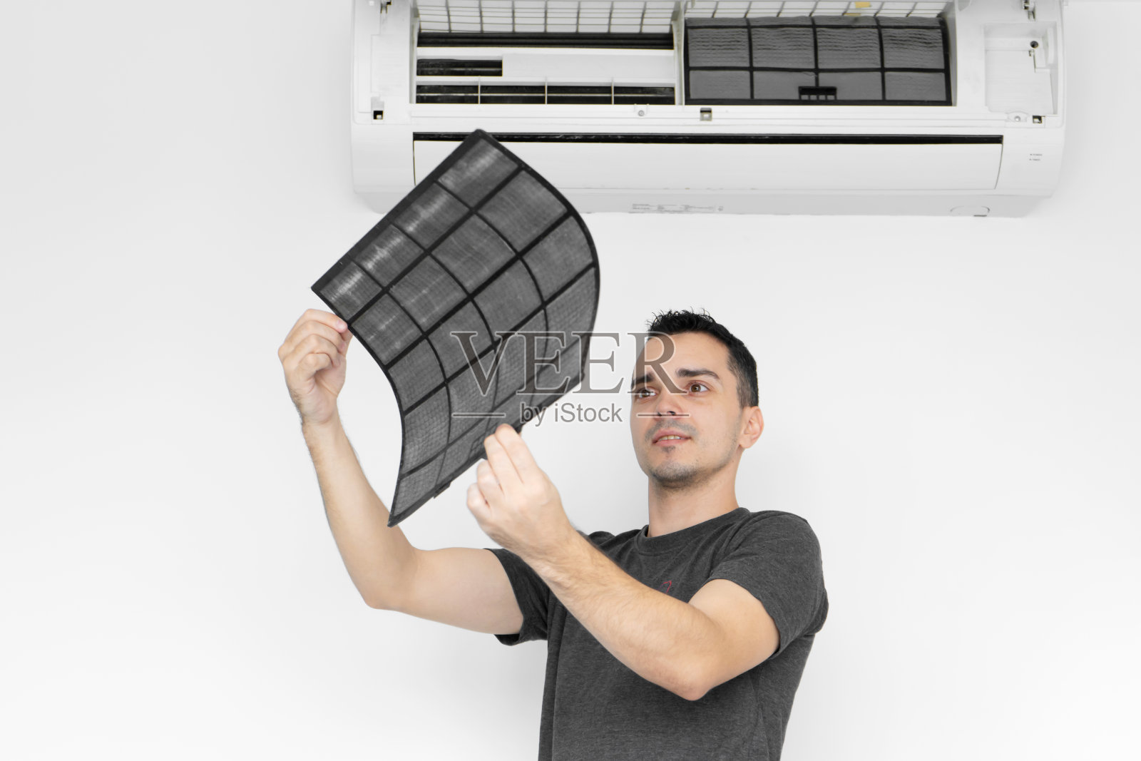 那家伙清理家用空调过滤网的灰尘。那家伙偷了一个很脏的空调过滤器。在他的手中检查它。气候保健设备。照片摄影图片