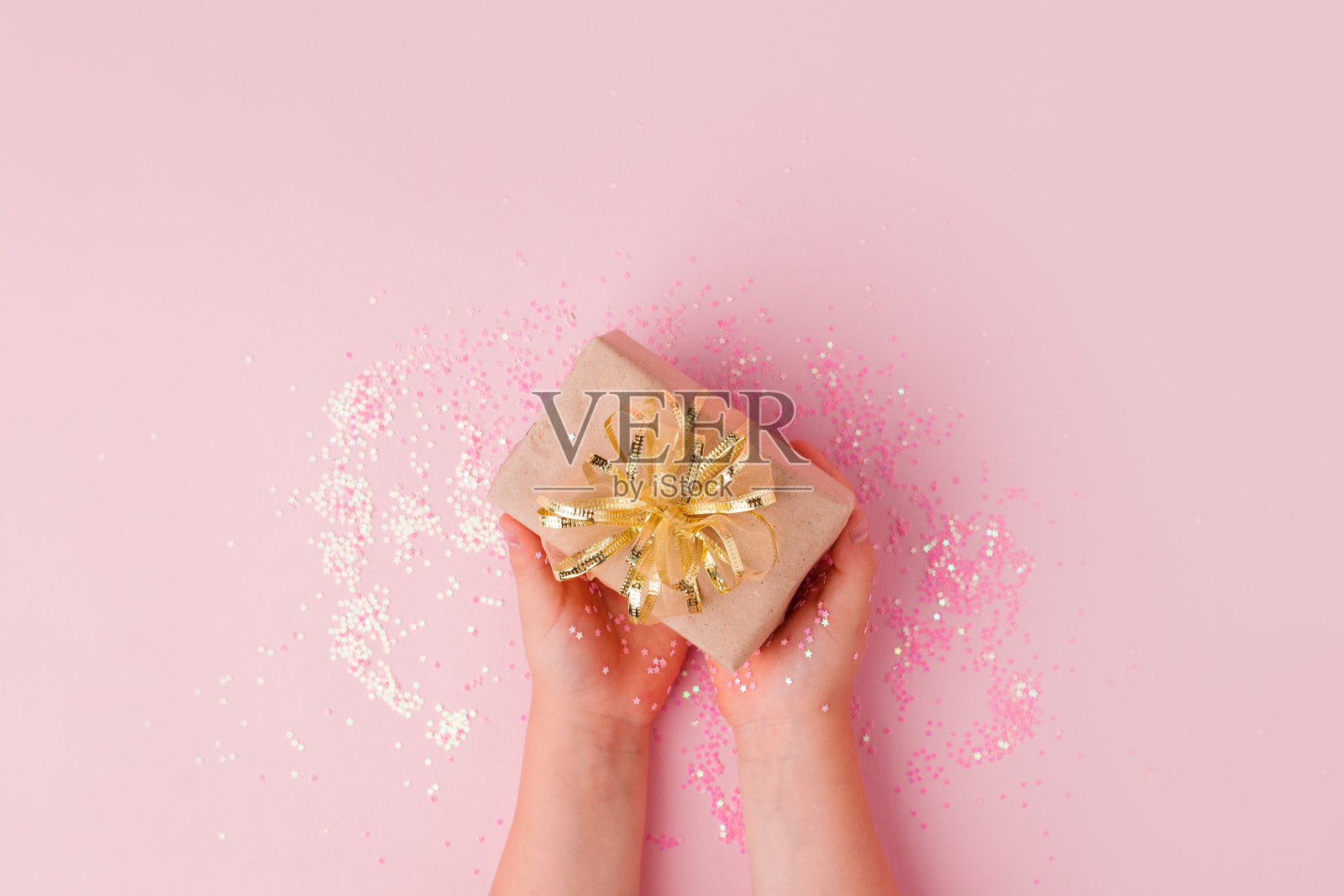 孩子们手握礼物与金色的蝴蝶结在柔和的粉红色的背景。节日背景:生日，情人节，母亲节，圣诞节，新年。平铺风格，销售购物照片摄影图片