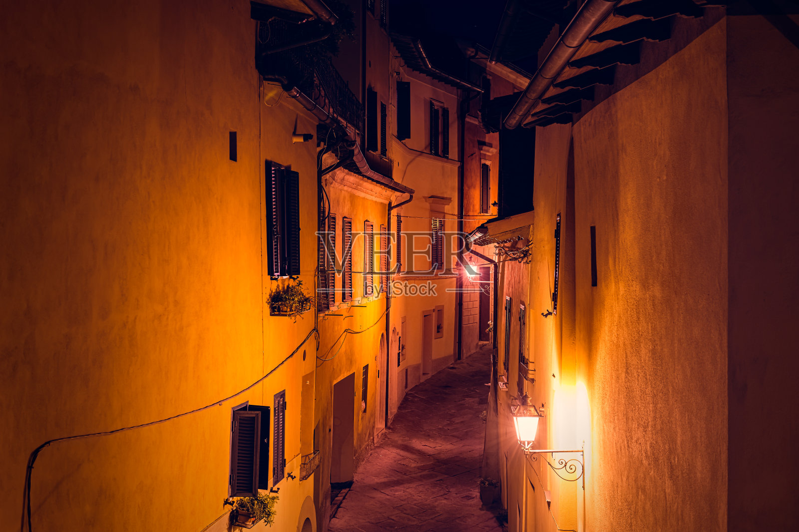 意大利Chiusi的街道狭窄的小巷和阳台窗户上的猫在托斯卡纳的历史小镇小村庄在夏夜与没有人的橘黄色灯照明照片摄影图片