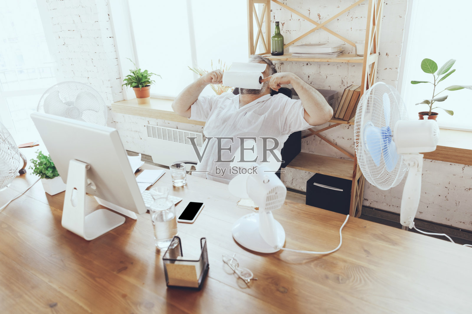 商人、经理在办公室里用电脑和电扇降温，感觉很热，脸红了照片摄影图片