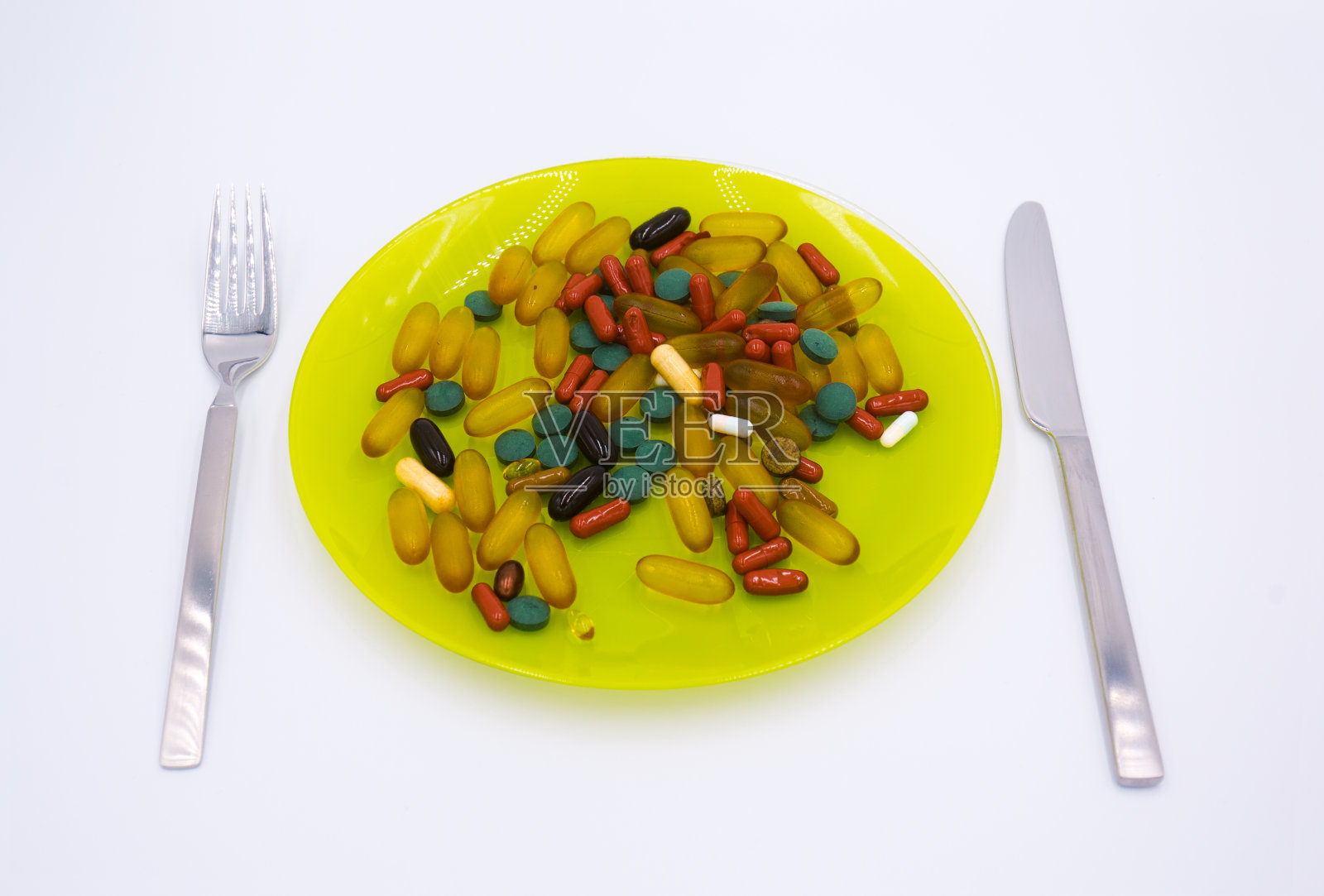 许多不同的减肥药和补品作为食物用刀叉放在绿色的盘子里照片摄影图片