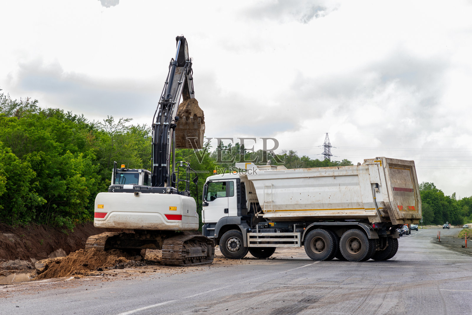 许多重型重型工业道路施工机械在新公路道路施工现场晴天以蓝天为背景。自卸车和挖掘机建造高速公路照片摄影图片