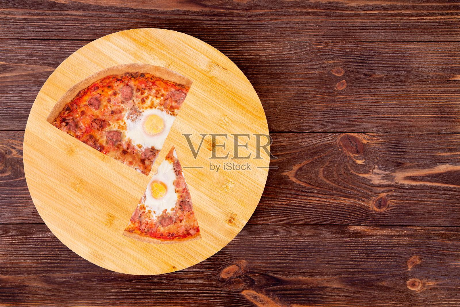 一块四分之一的美味披萨配上牛肉香肠、鸡蛋和培根，放在一张简陋的木头桌子上，复制空间照片摄影图片