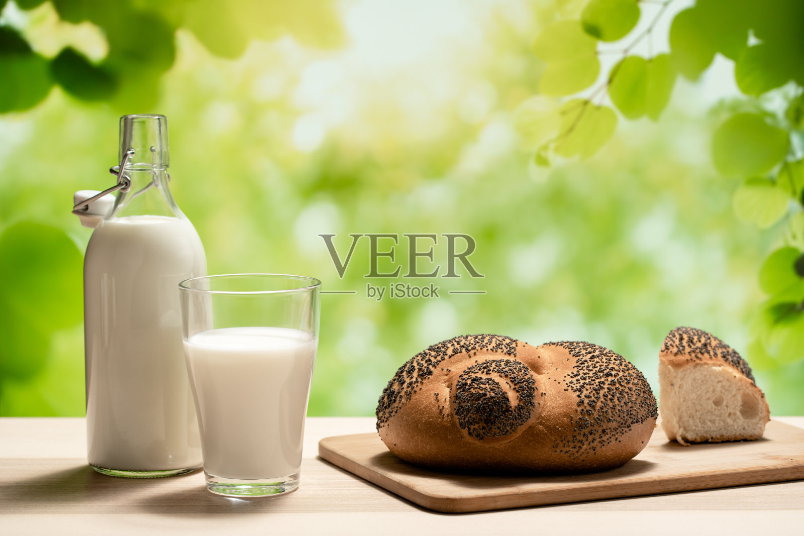 切菜板上放着一瓶牛奶、一只玻璃杯和一条面包照片摄影图片