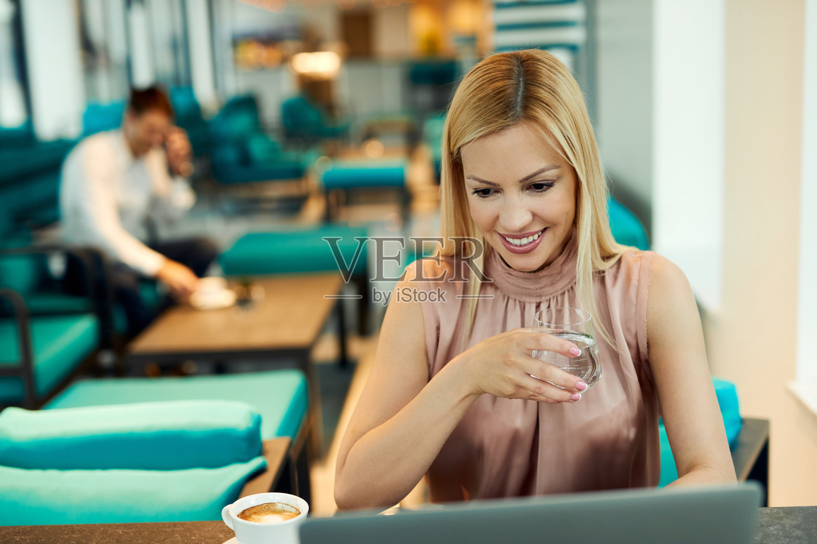 在咖啡馆用笔记本电脑的时候喝杯水的快乐女人。照片摄影图片