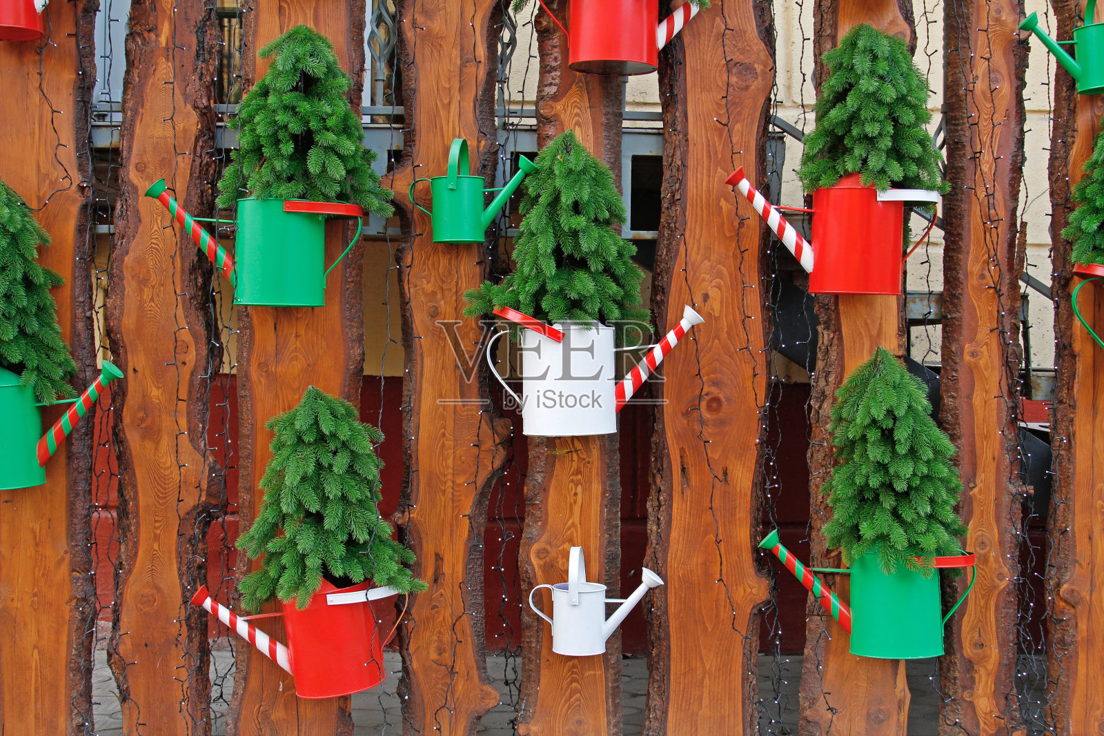 人工针叶树在五颜六色的浇水罐上挂在木栅栏上，还有一个花环照片摄影图片