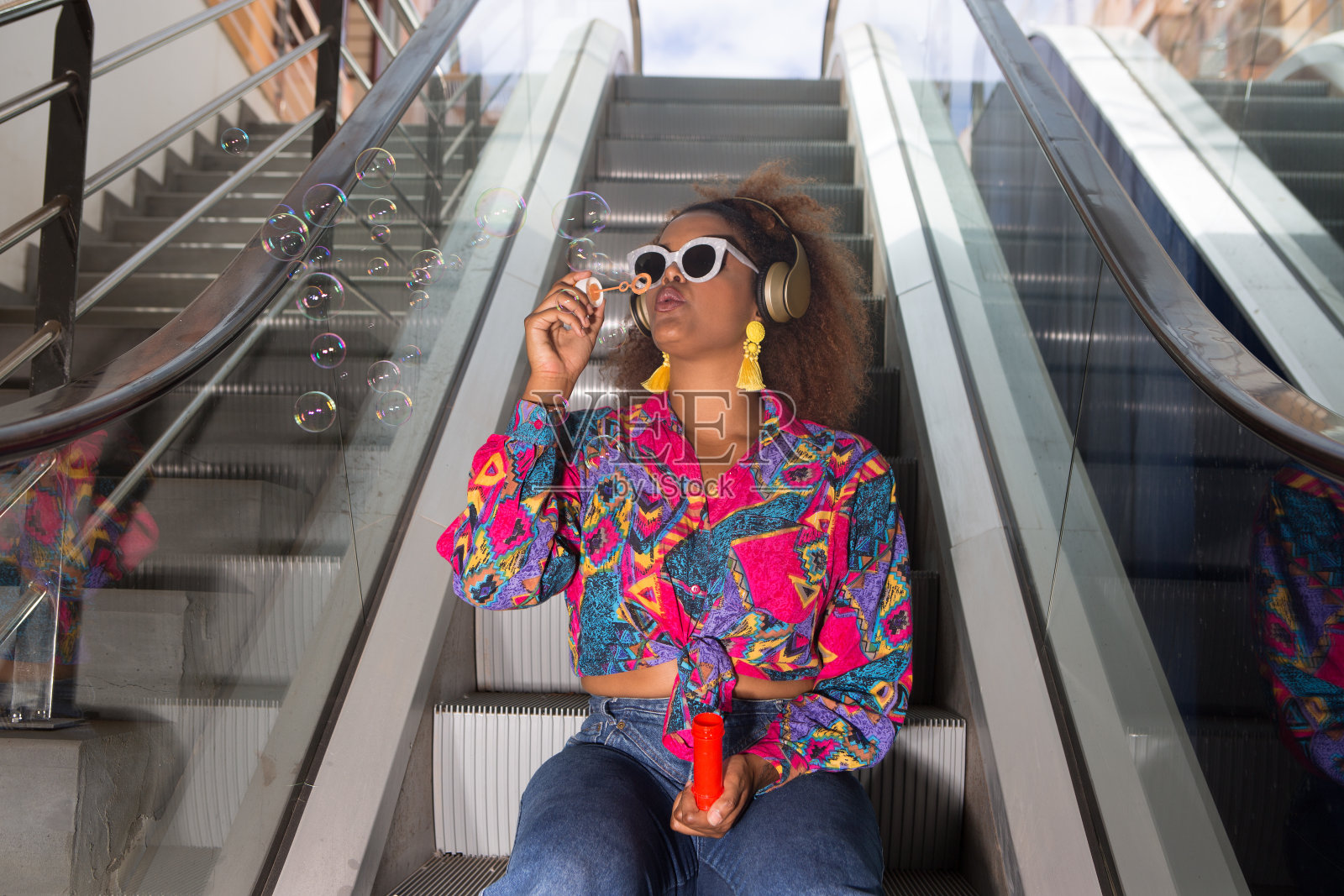 戴耳机的黑人妇女坐在可移动的楼梯上吹泡泡照片摄影图片