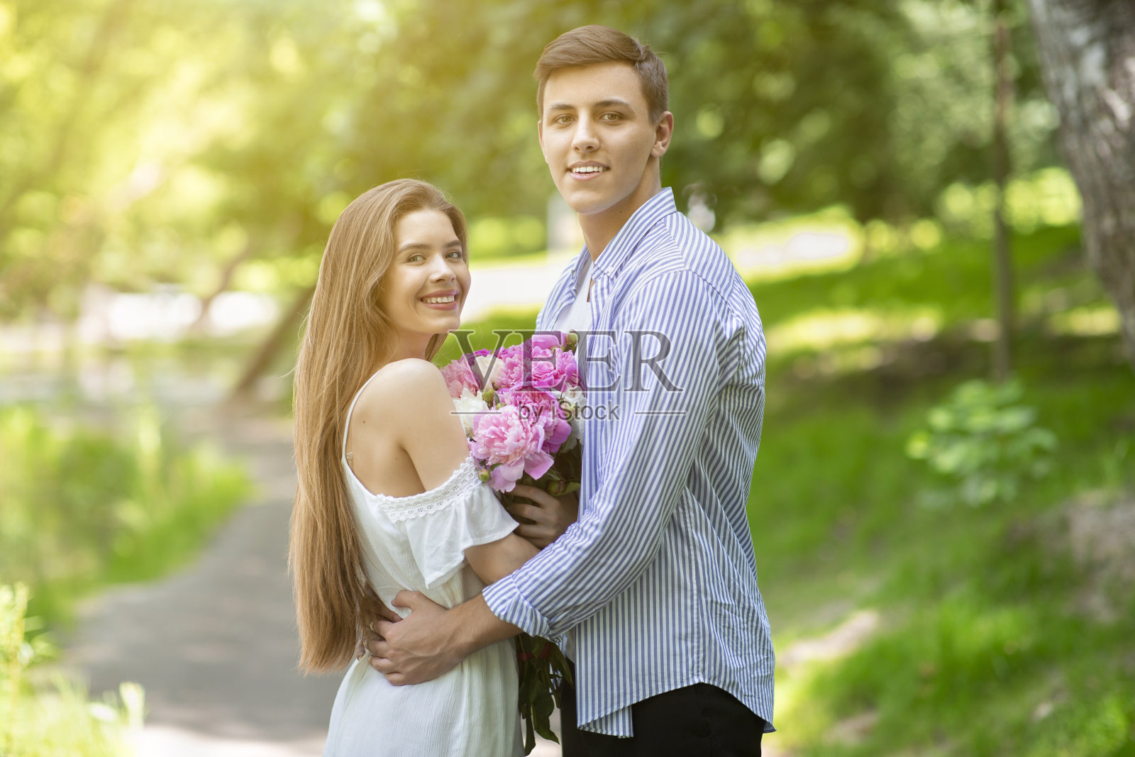 生日庆祝活动。在阳光明媚的日子里，一对深情的情侣抱着一束可爱的牡丹花在公园里拥抱照片摄影图片