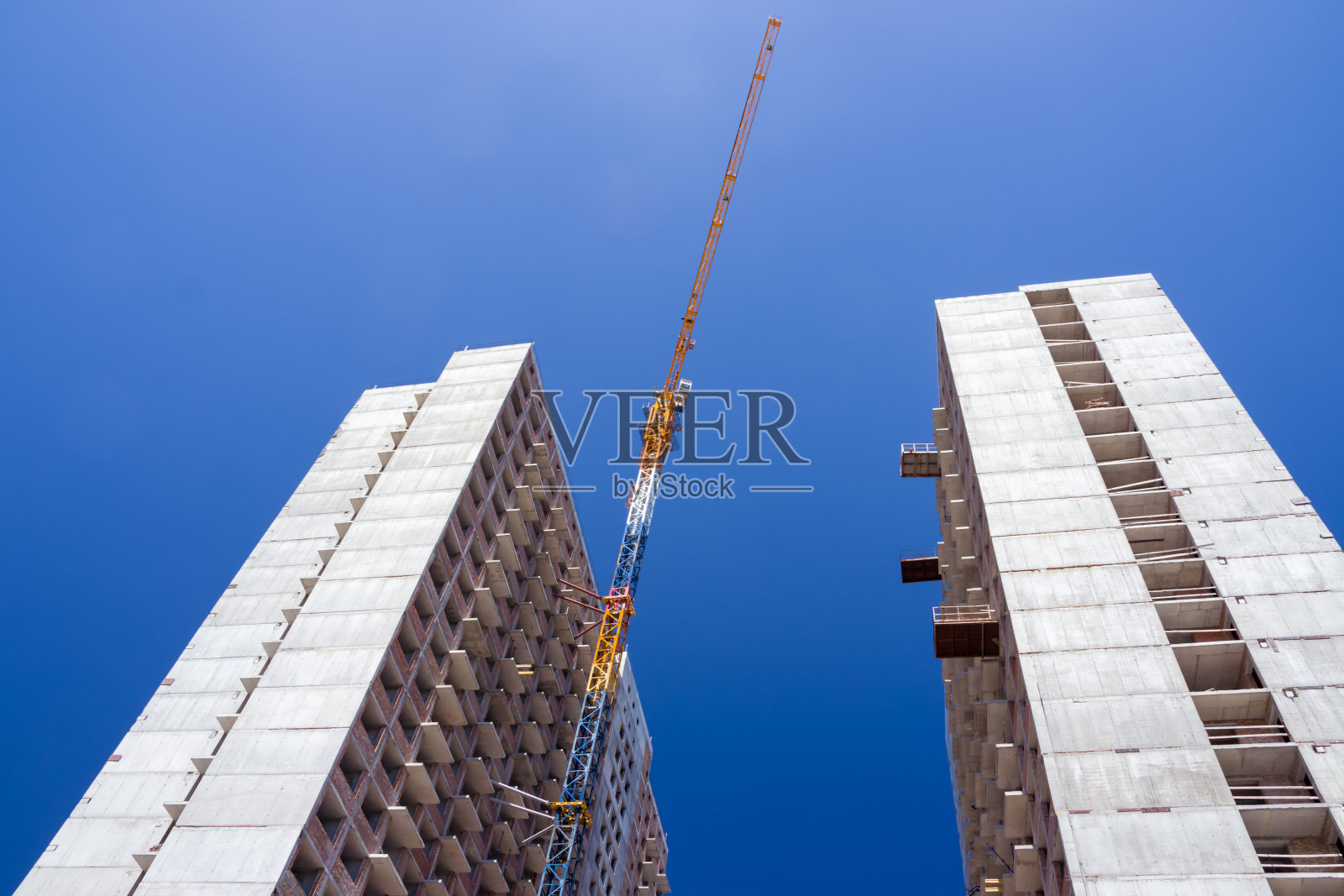 一个承包商用起重机建造了一座高大的房子。在无云的蓝天背景下的房子的照片。房屋施工，施工起重机，未完工的房屋照片摄影图片