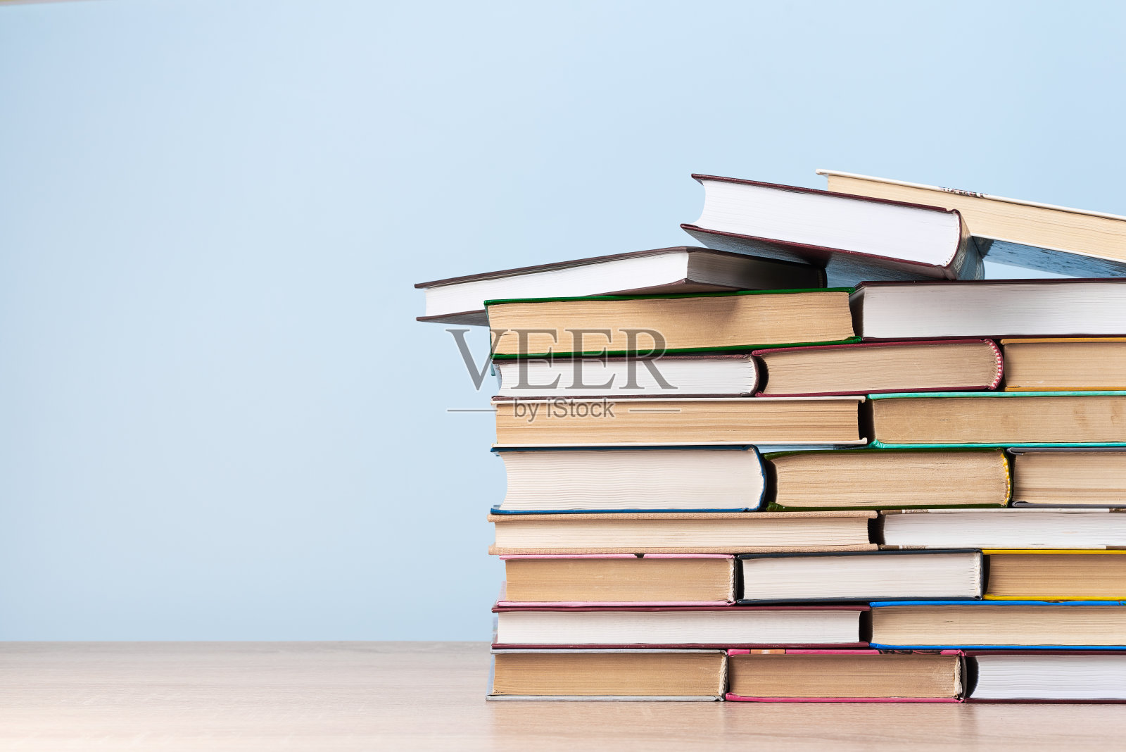 淡蓝色的墙上放着一张木桌，上面放着一大堆书照片摄影图片