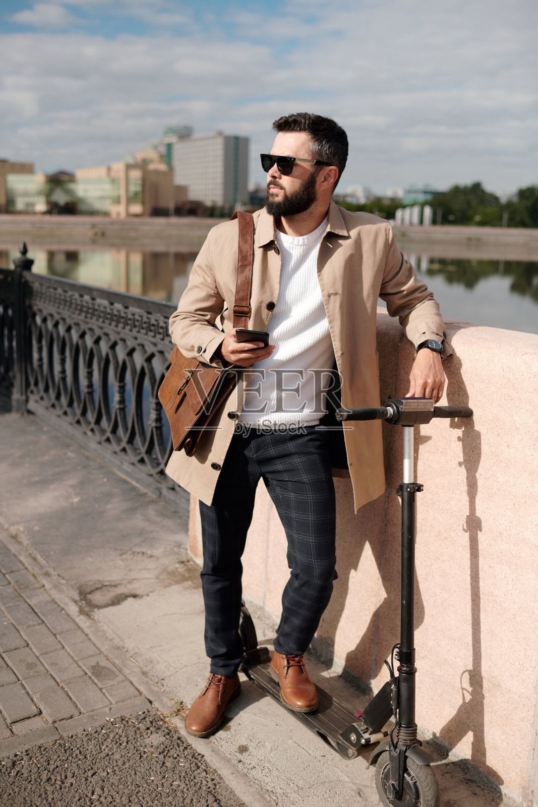 年轻男子穿着优雅时尚的休闲装，戴着墨镜站在河边照片摄影图片