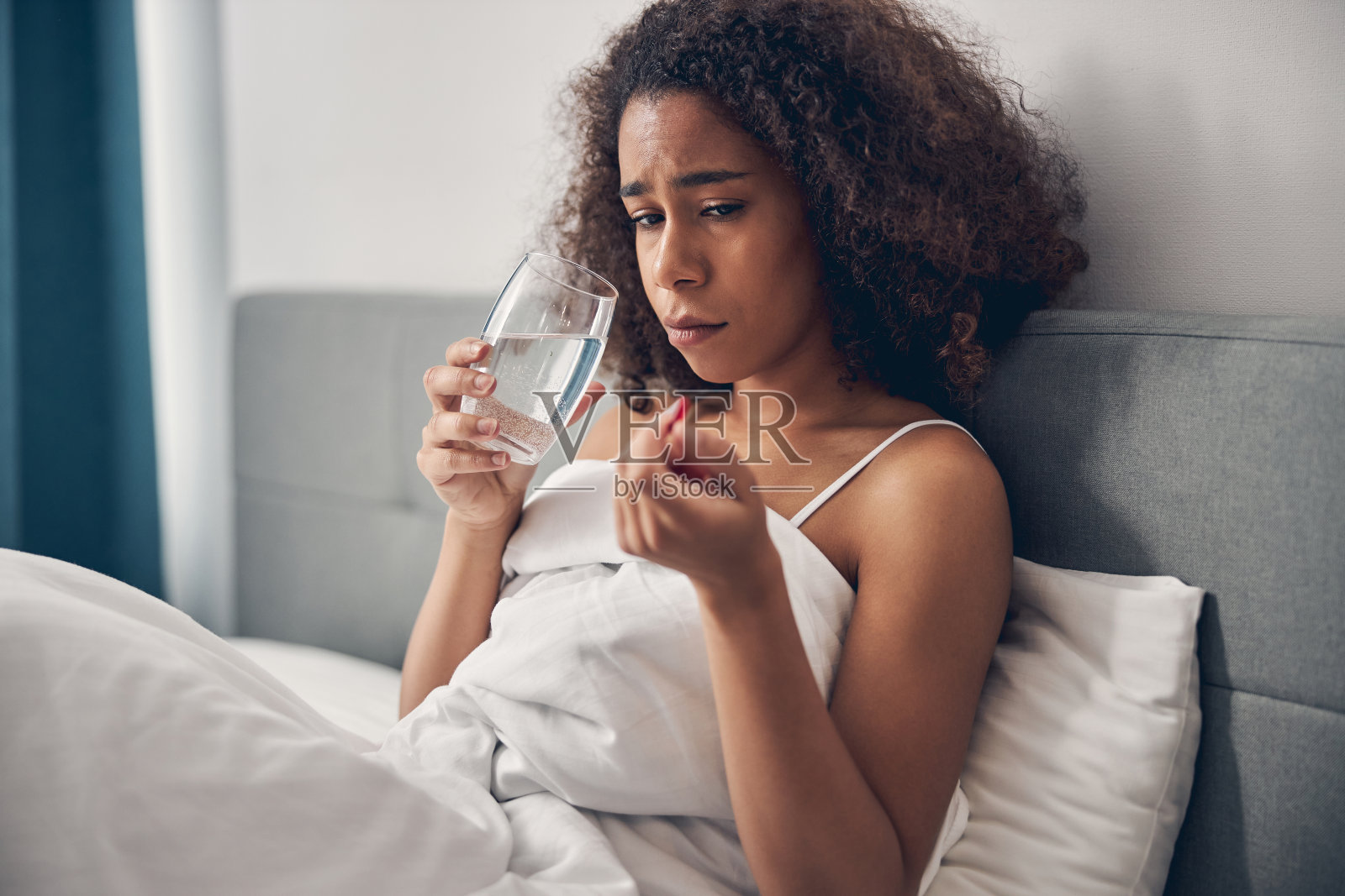 无精打采的黑头发年轻女士坐在床上照片摄影图片