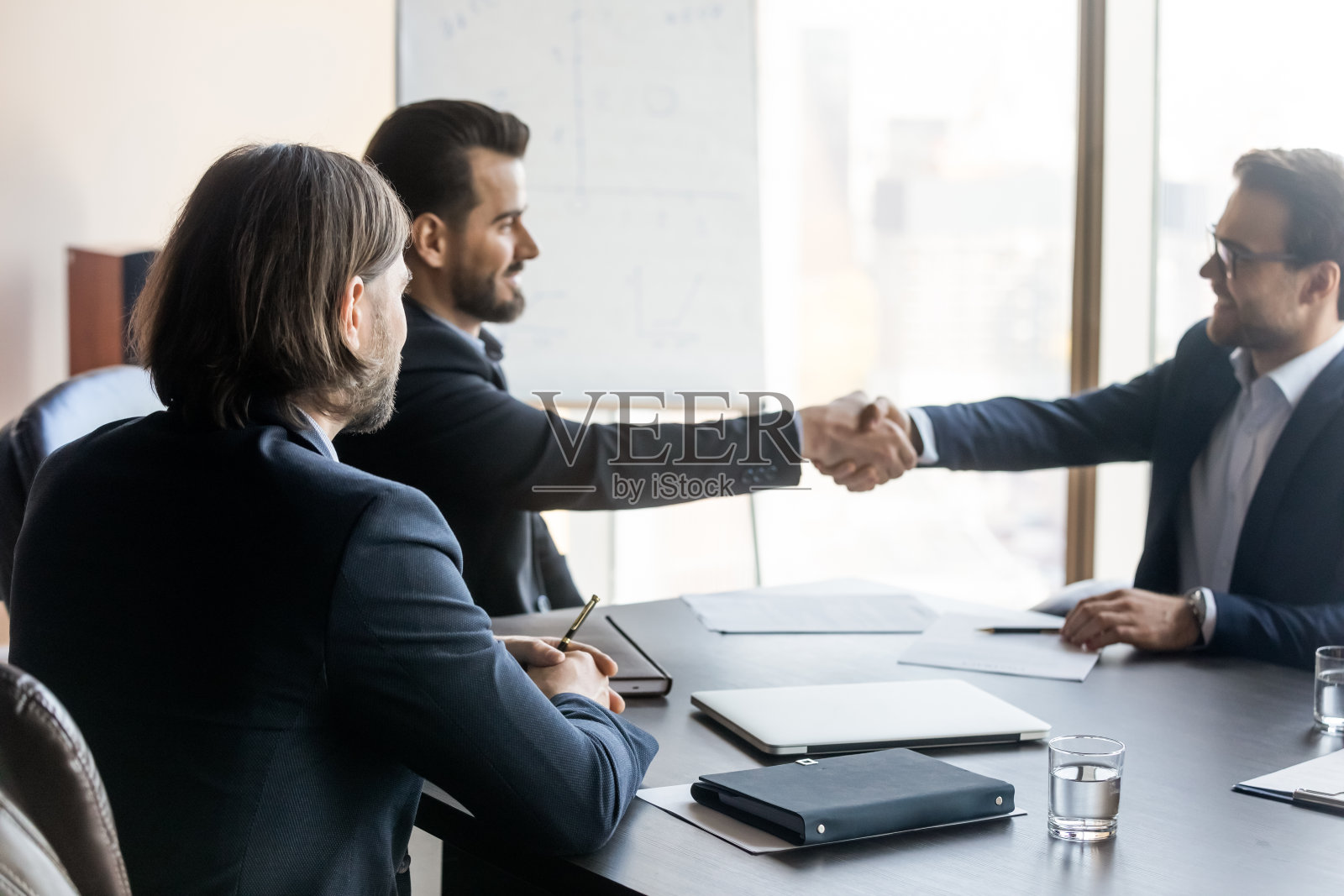 快乐的商人看着两个自信的男性伙伴握手。照片摄影图片