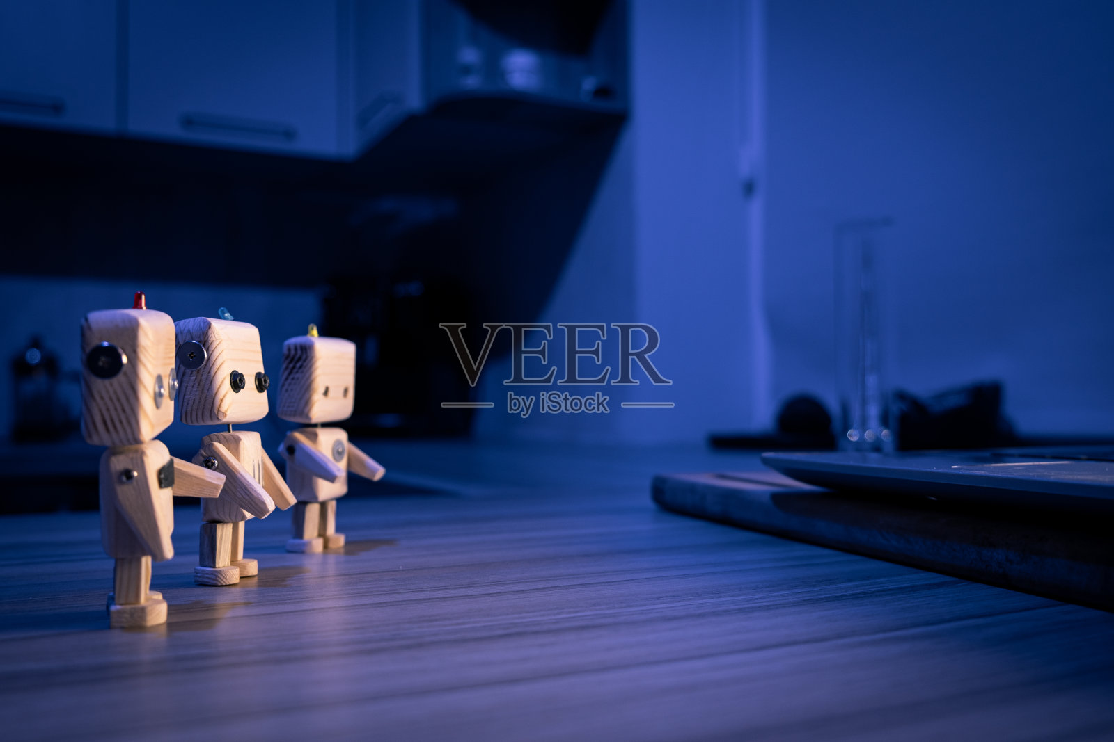 一个小的木制机器人玩具在黑暗中看着笔记本电脑。墙纸,长途跋涉的背景。低光照片摄影图片