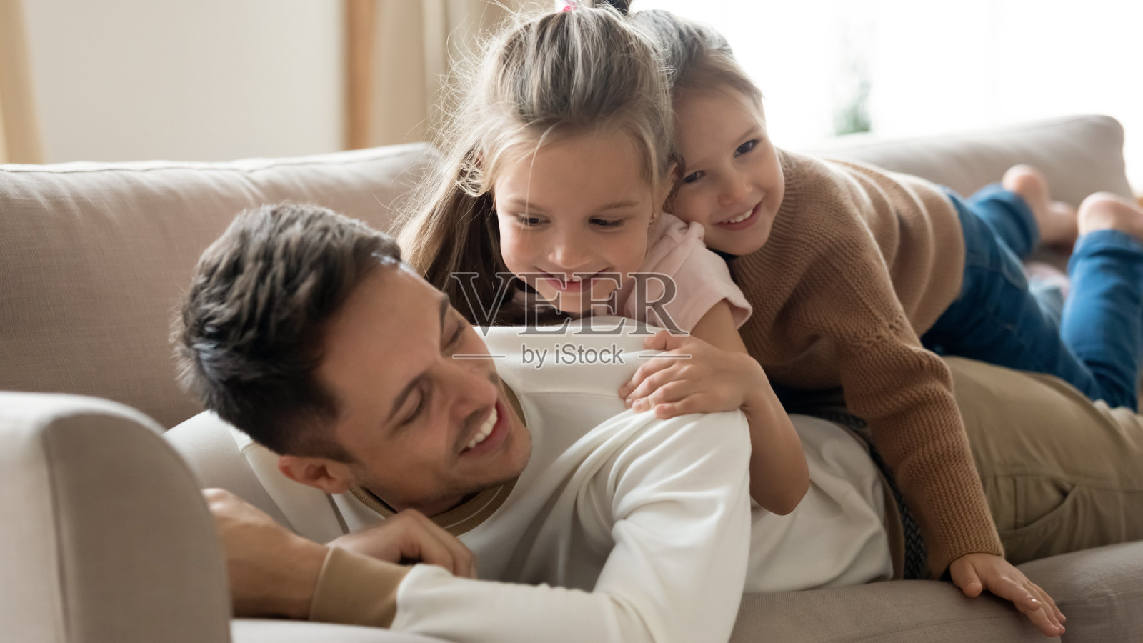 快乐的父亲和两个在沙发上休息的小女儿照片摄影图片