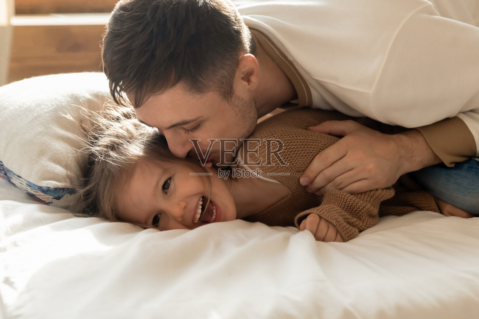慈爱的父亲亲吻躺在床上可爱的小女儿照片摄影图片