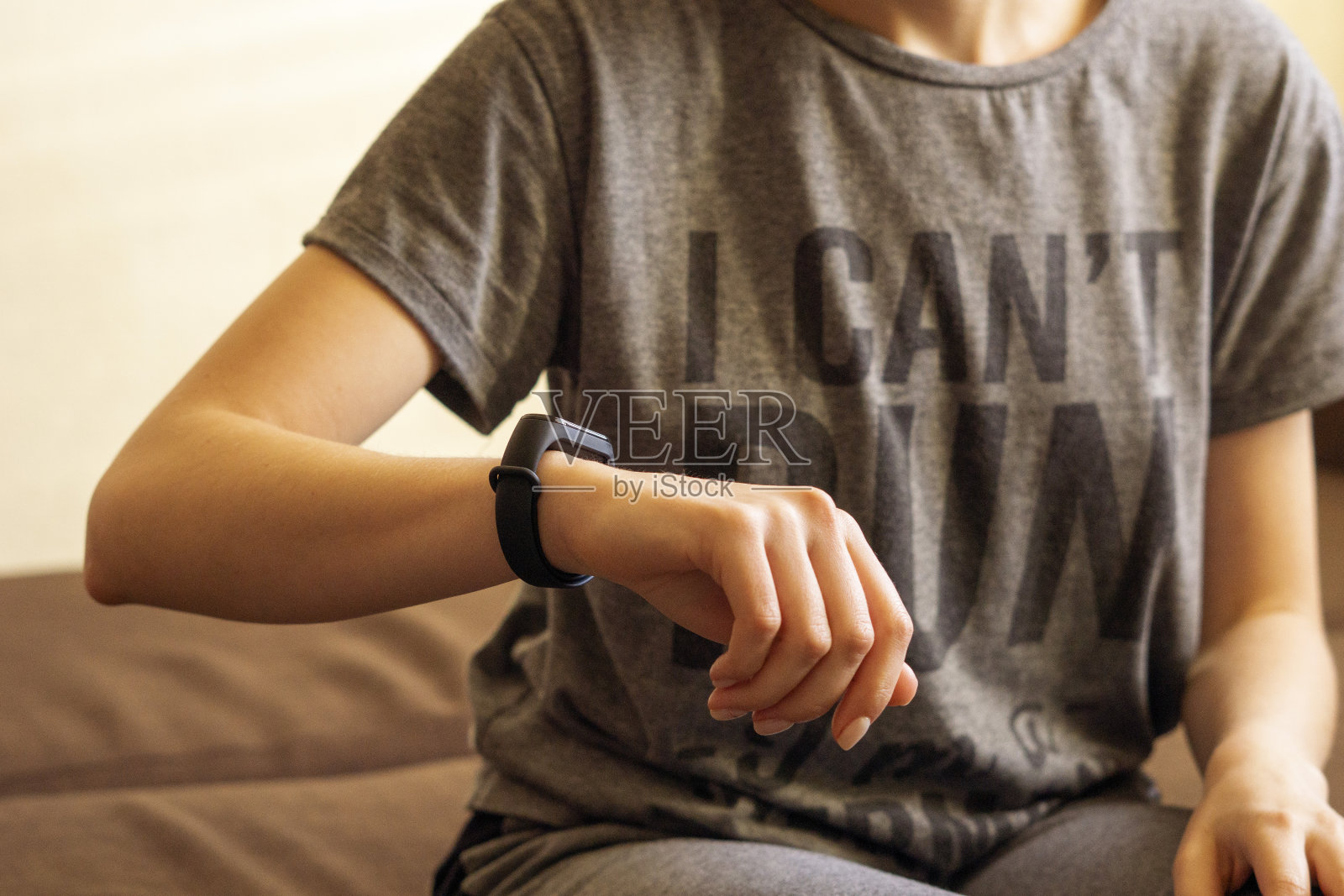 一个年轻女人坐在沙发上看一个腕上的小玩意儿的特写。科技在现代生活中，活动检查，健康保养的理念。照片摄影图片