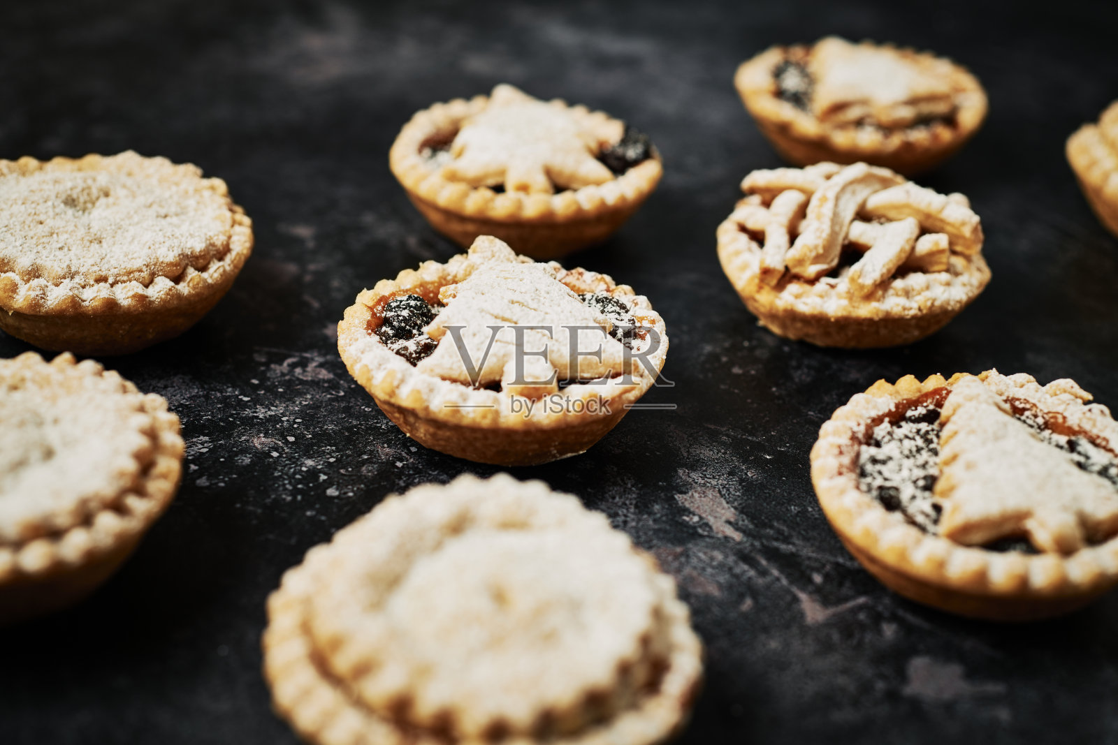 在黑色纹理的背景下，撒上糖霜的一排排自制肉馅饼。照片摄影图片