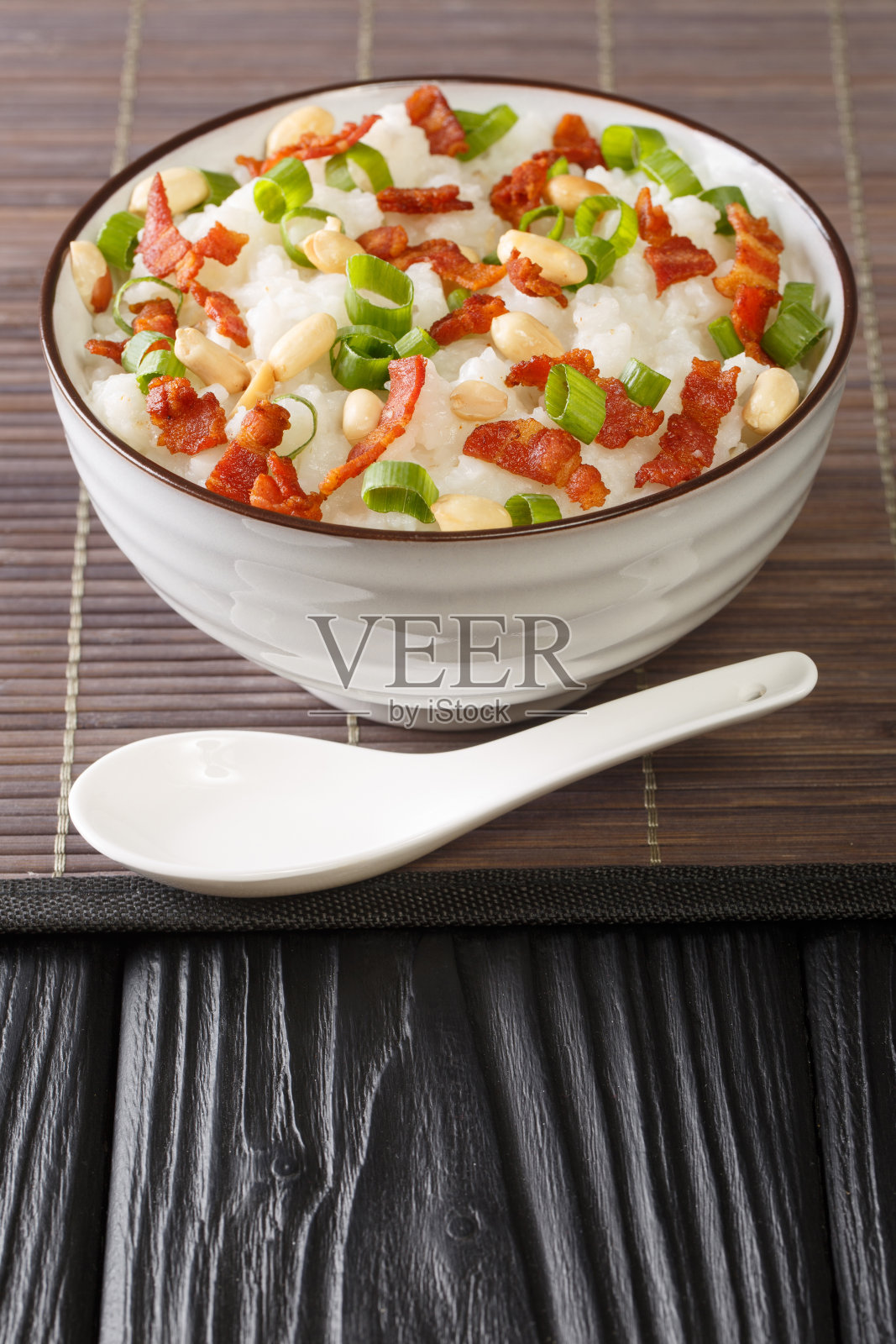 在中国的烹饪中，粥(jook)用大量的水在碗中煮茉莉花米饭，加入培根，花生和大葱。垂直照片摄影图片