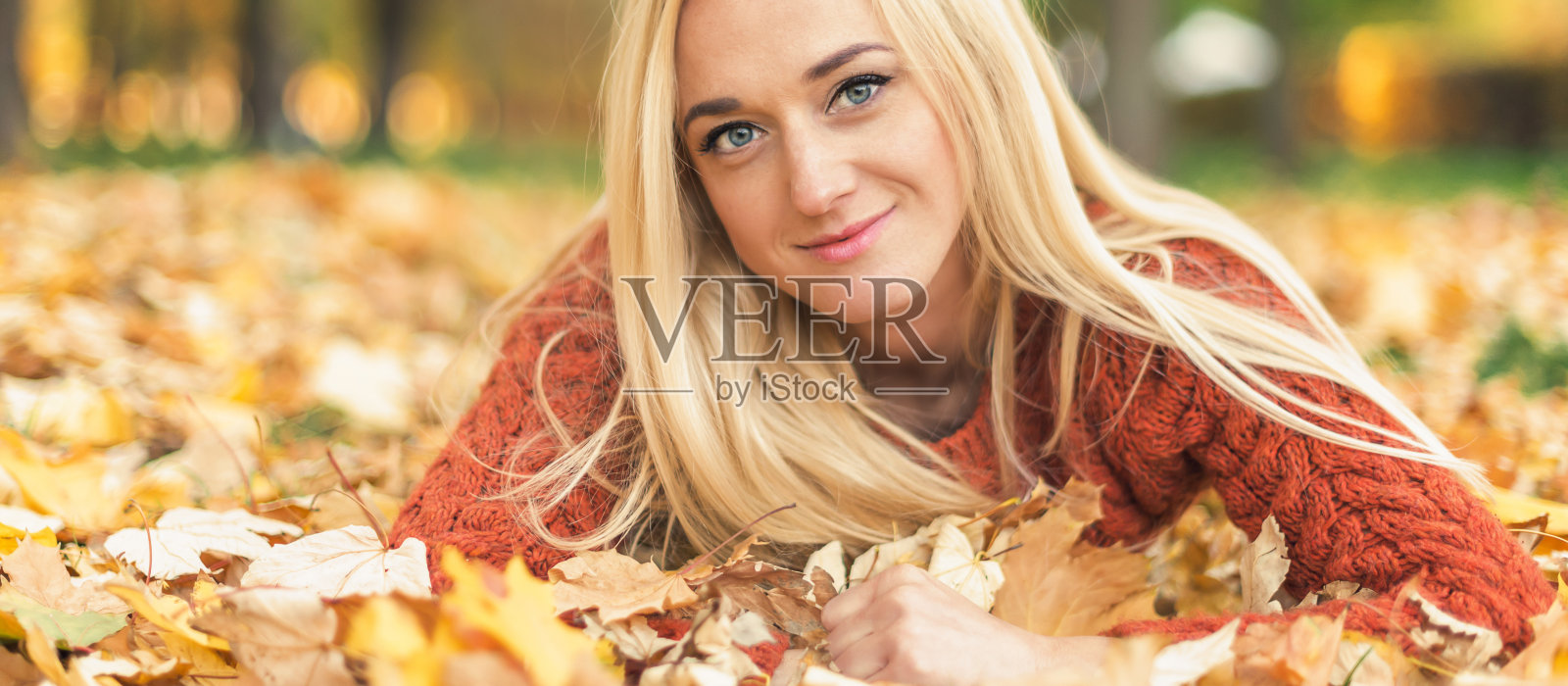 在秋天的公园里，一个女人躺在树叶上照片摄影图片