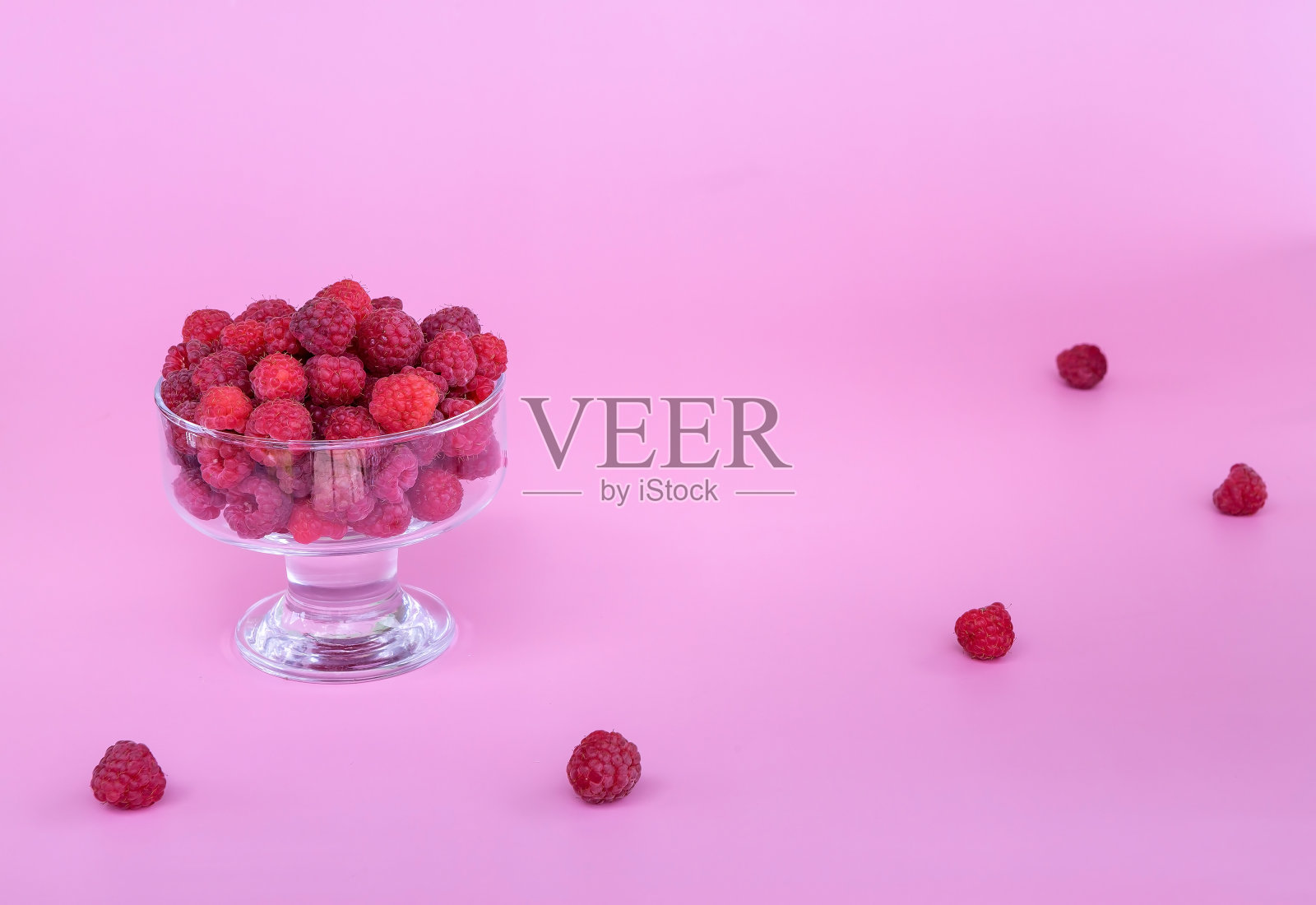 熟透的新鲜覆盆子放在一个玻璃花瓶里，在粉红色的背景上照片摄影图片