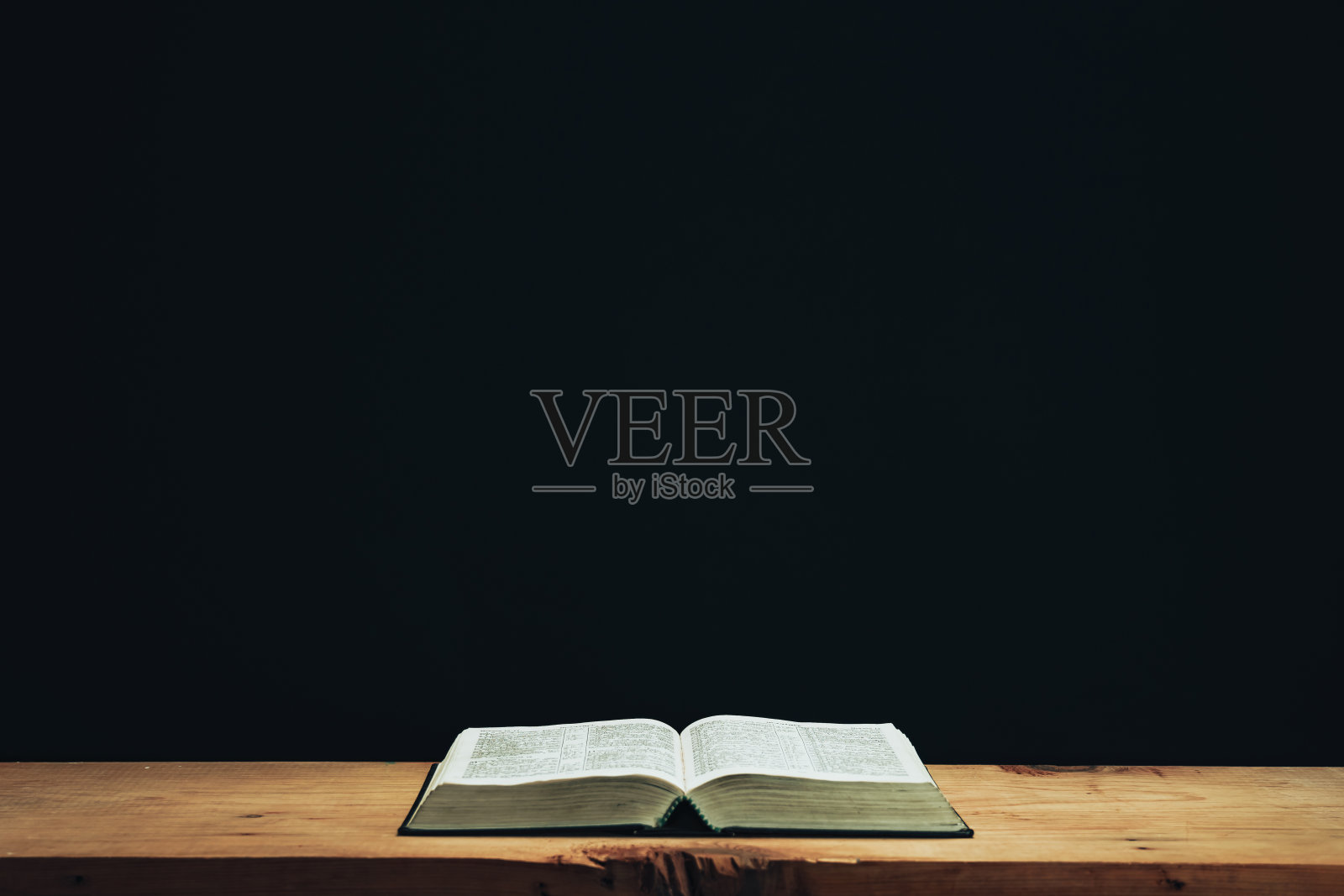 在一张红色的旧木桌上打开圣经。美丽的黑色墙壁背景。照片摄影图片