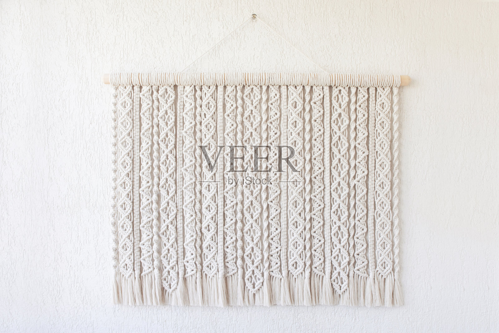 手工刺绣的。100%纯棉墙面装饰用木棒挂在白色墙面上。流苏编织和棉线。女性的爱好。环保的现代编织DIY自然装饰理念在室内照片摄影图片