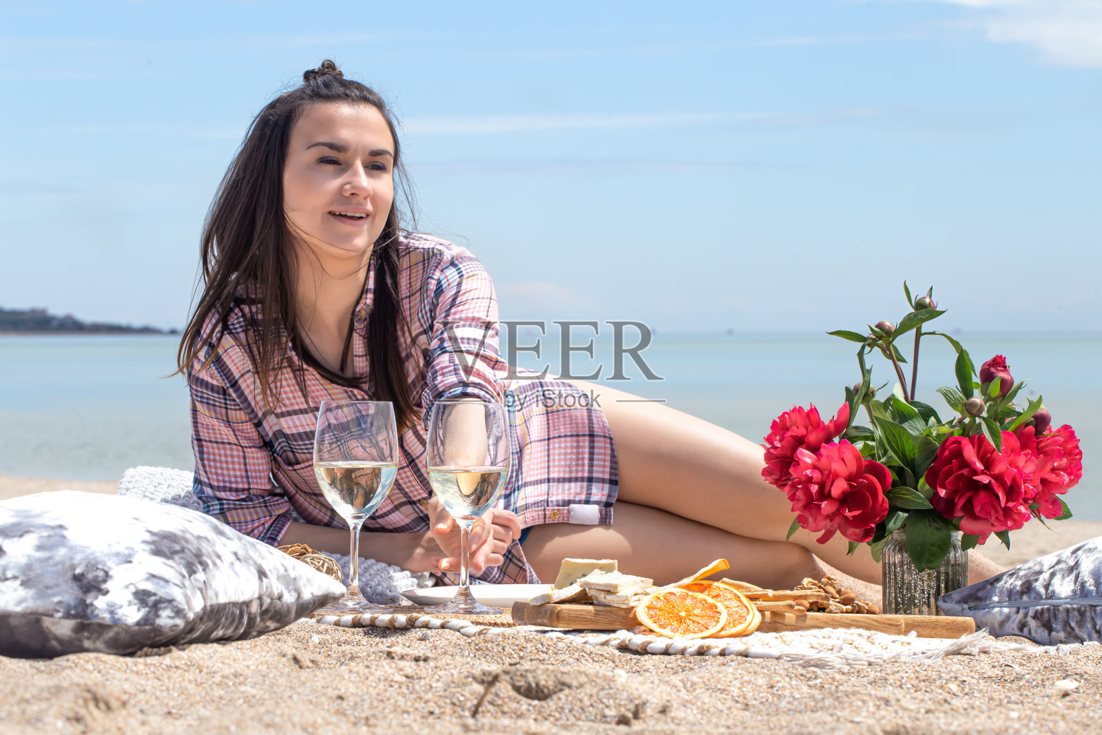 一个女孩正在海滩上休息。在沙滩的沙滩上浪漫的野餐。以鲜花和饮料为背景。照片摄影图片