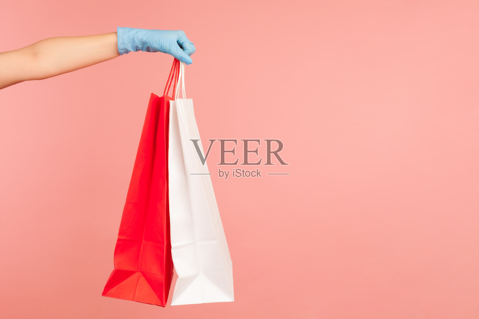 侧面特写的人的手在蓝色的外科手套拿着和显示红色和白色的购物袋。照片摄影图片