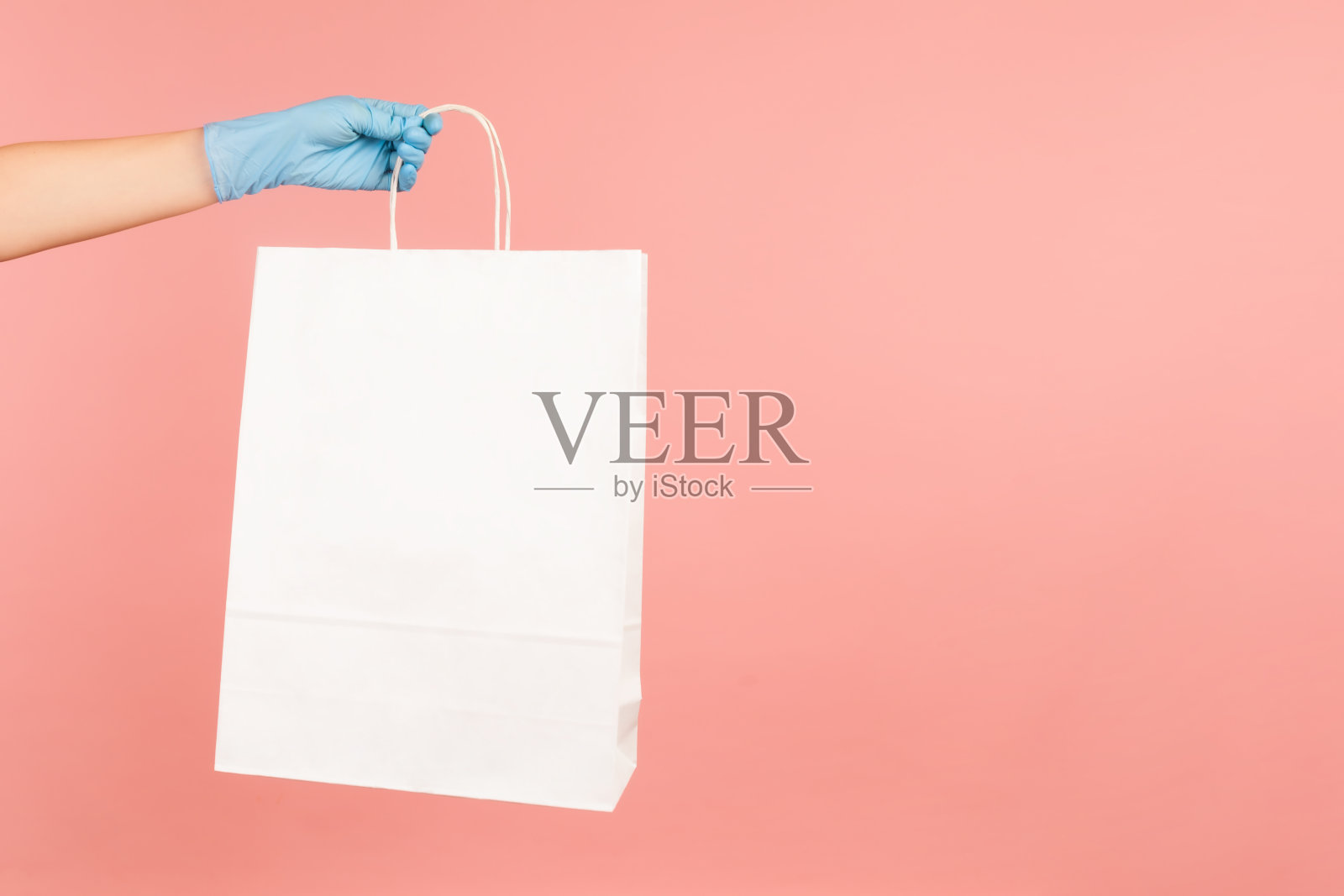 侧面特写的人的手在蓝色外科手套拿着和显示白色购物袋。照片摄影图片