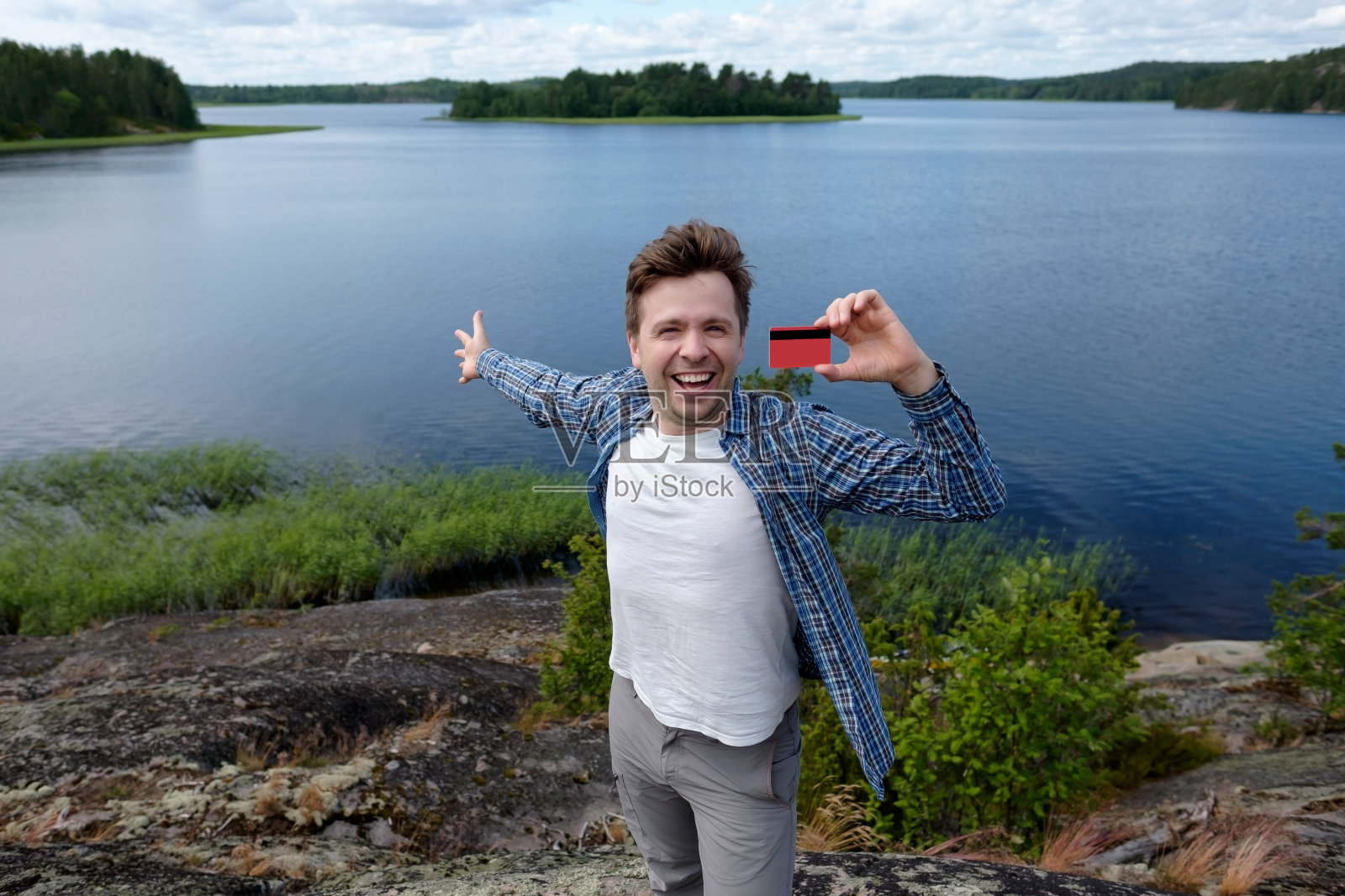 微笑的男性显示空的信用卡。他站在湖边。照片摄影图片