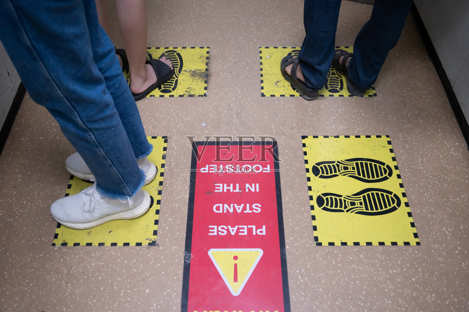 在新冠肺炎大流行期间，电梯或电梯内站在黄色脚印标志上的人的脚，为防止病毒传播预留空间。照片摄影图片