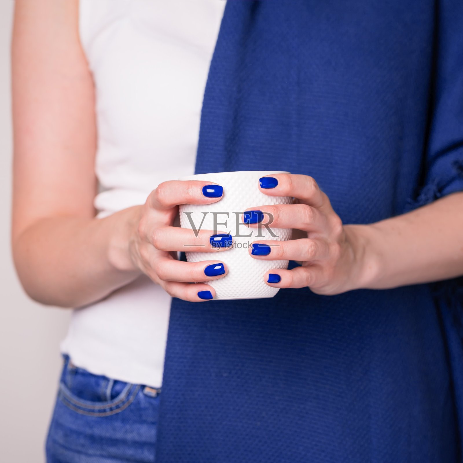 美丽的女性手中拿着白色的杯子。用蓝色指甲油修指甲。季节变化的概念照片摄影图片