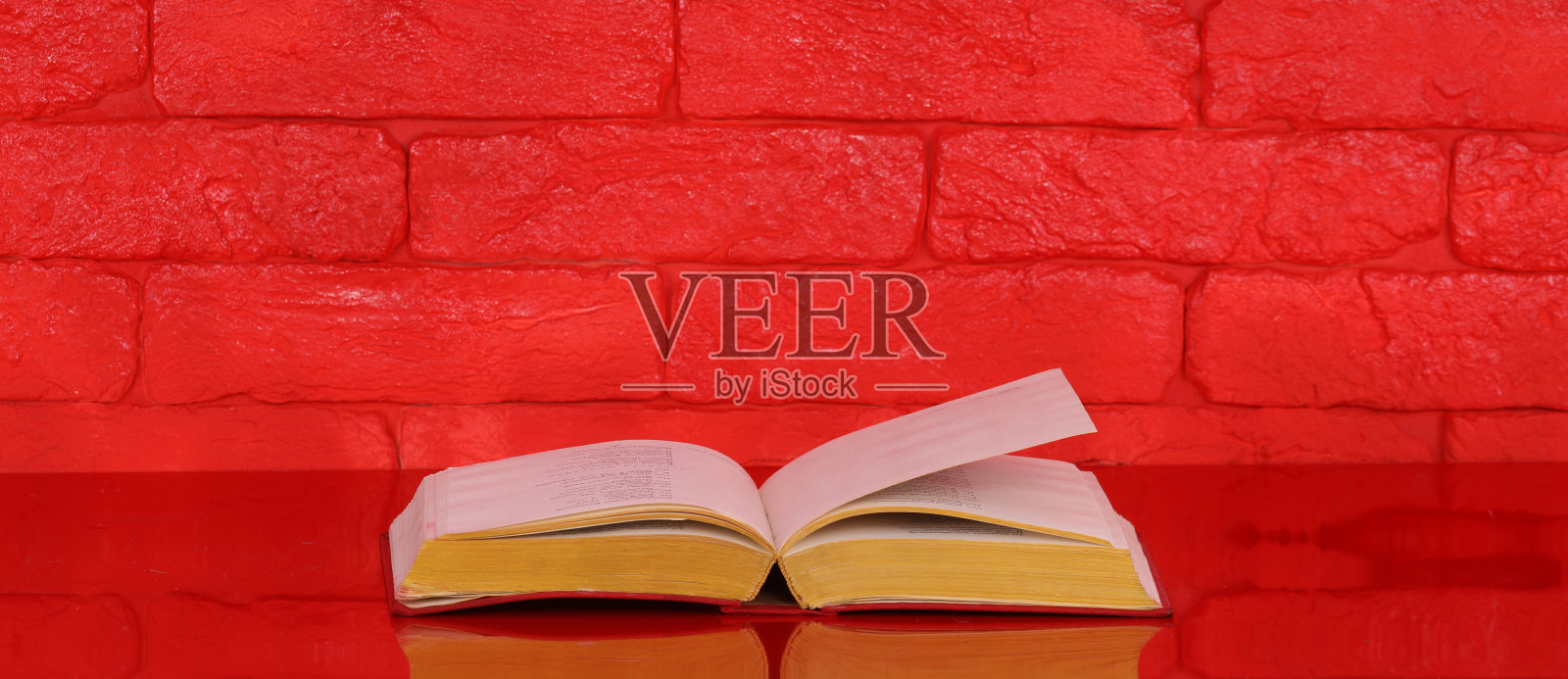 翻开书在红桌上，红砖墙为背景照片摄影图片